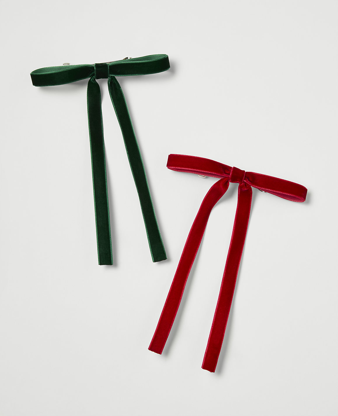 Two velvet bow ties, one green and one red, lie on a plain white background.