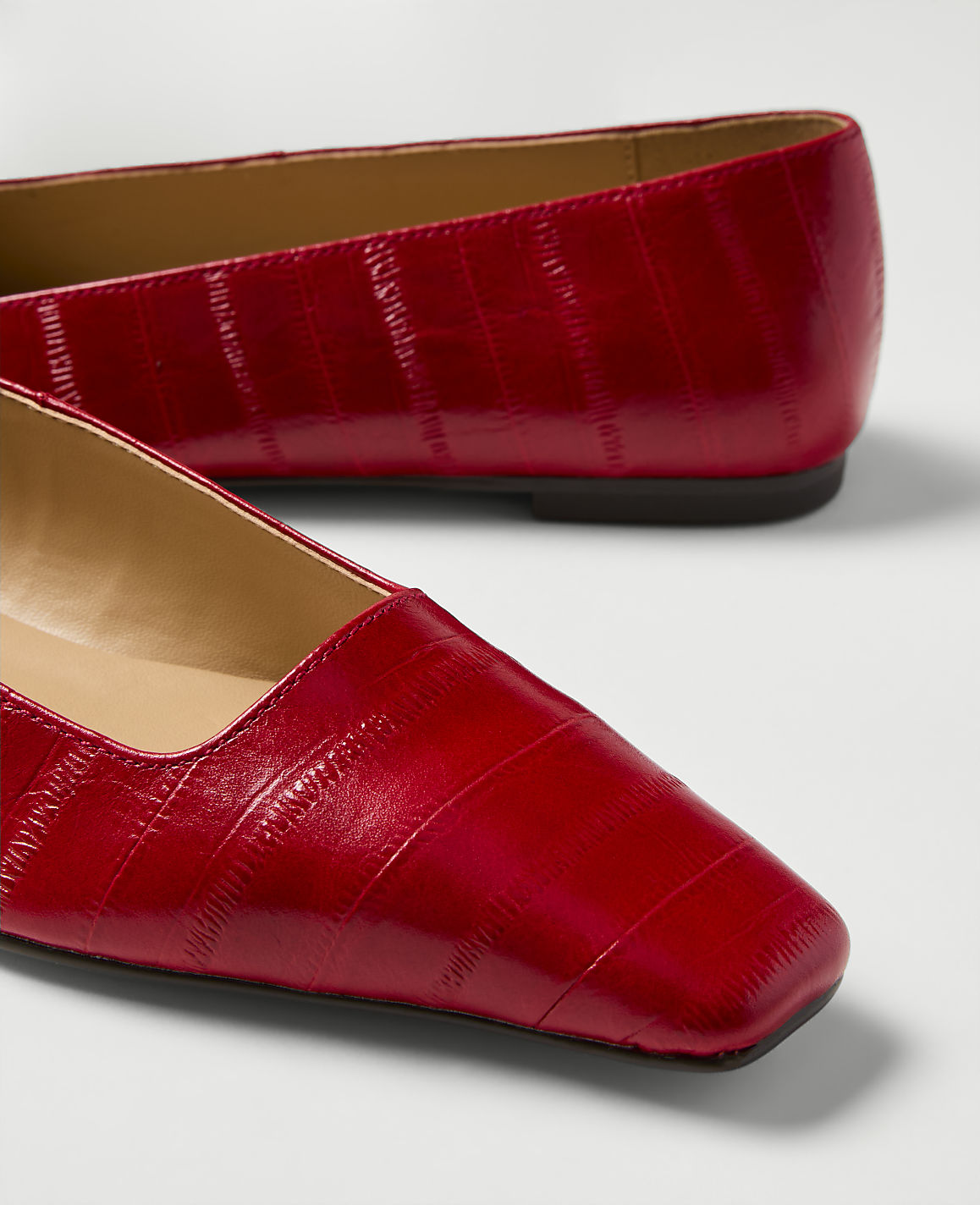 A pair of shiny red square-toe flats with a textured finish are displayed against a plain white background.