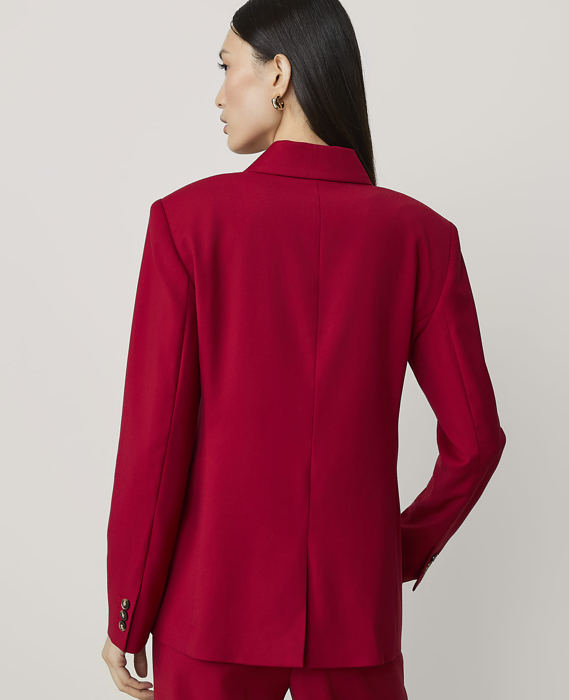 A woman in a red blazer stands against a plain, light-colored background.