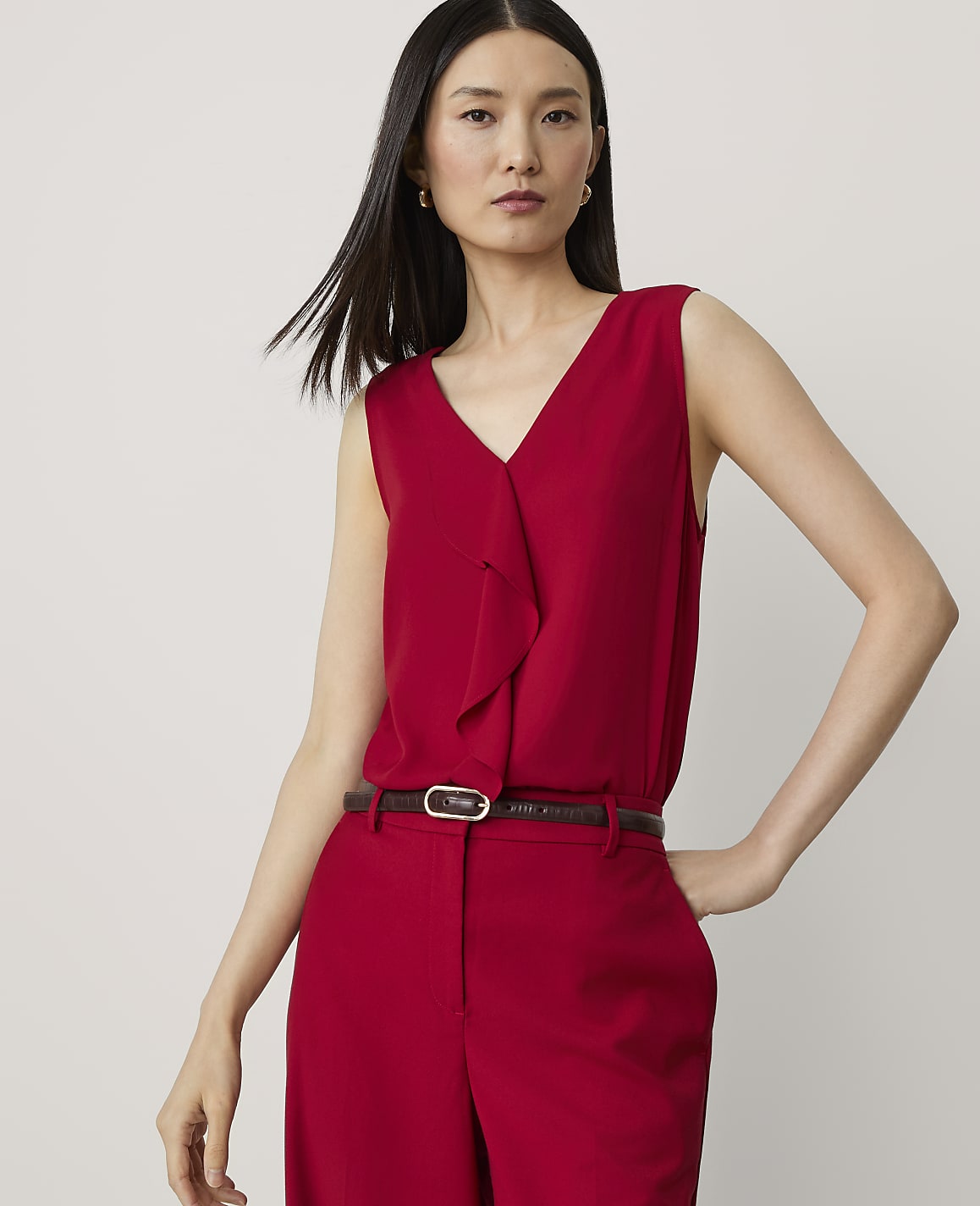 A woman in a red v-neck top and pants stands against a plain white background.