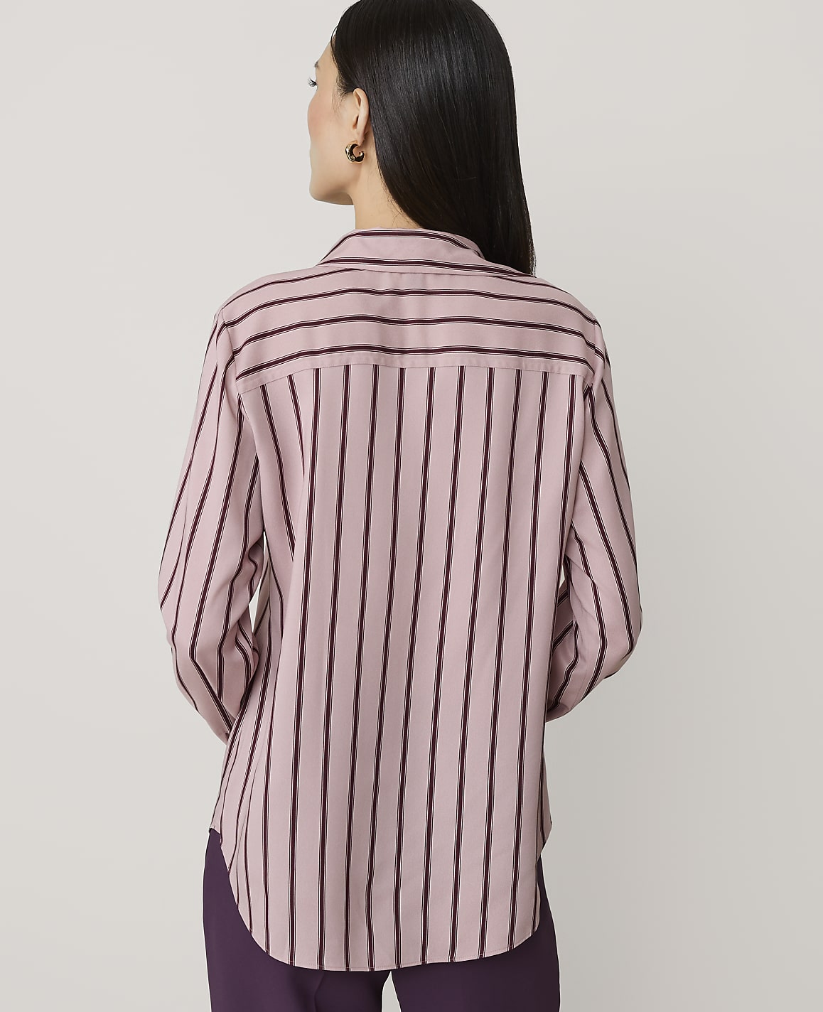 A woman in a pink and purple striped shirt stands against a plain, light-colored background.