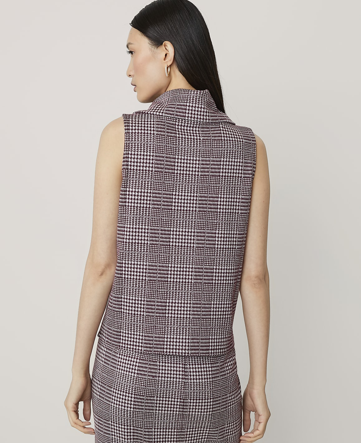 A woman in a plaid vest and skirt stands against a plain background.
