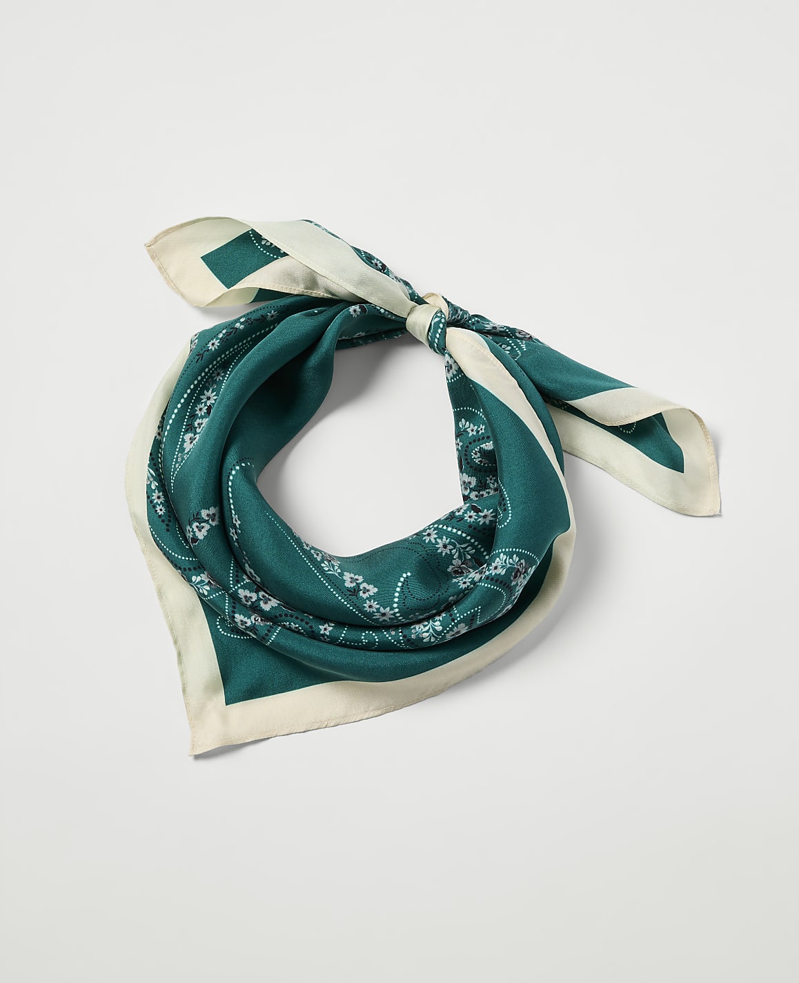A teal bandana with a white paisley pattern and cream trim is tied in a knot against a plain white background.