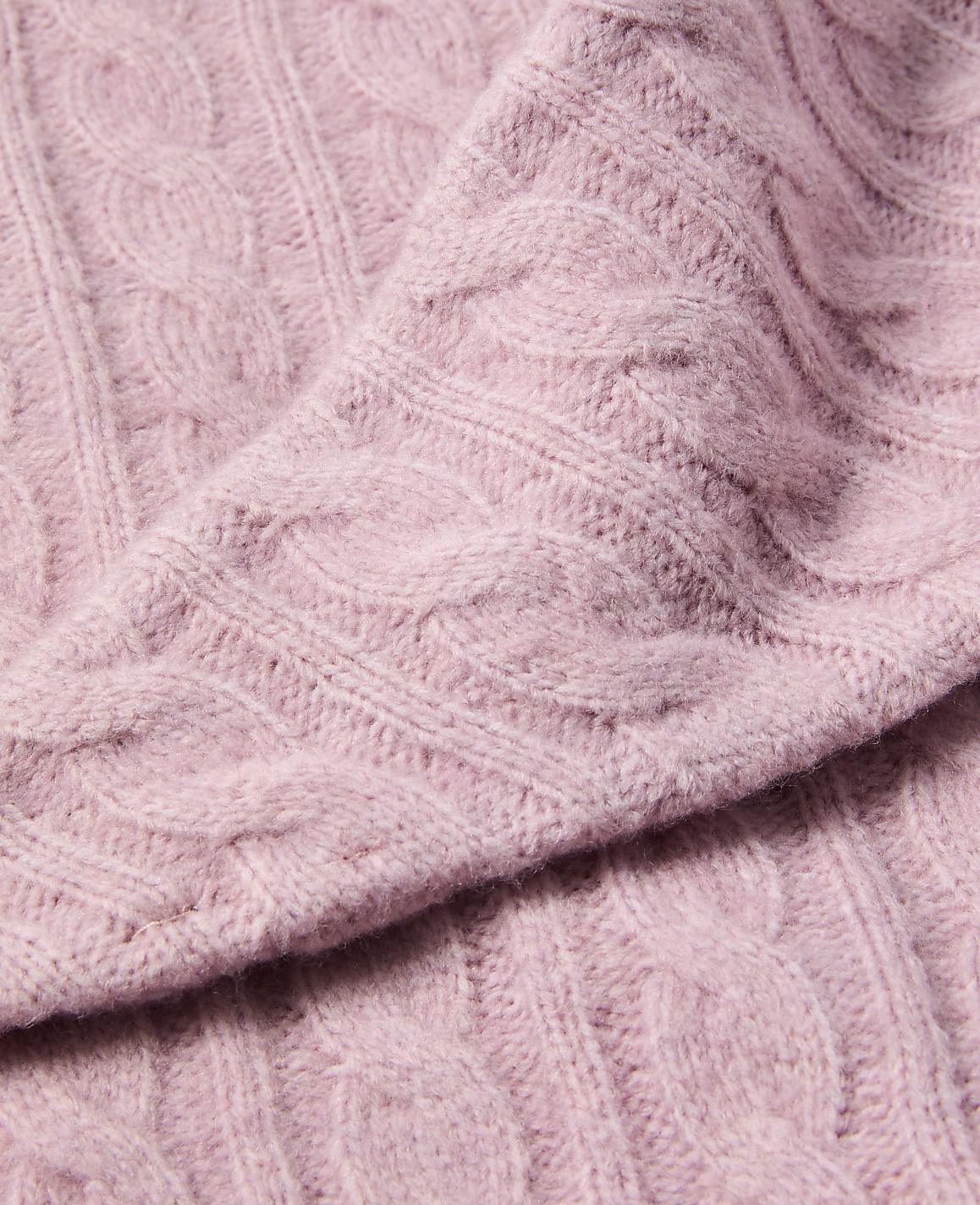 A close-up of a soft, pink cable-knit sweater fills the frame, with the textured fabric creating a cozy and inviting foreground against a subtly blurred background.