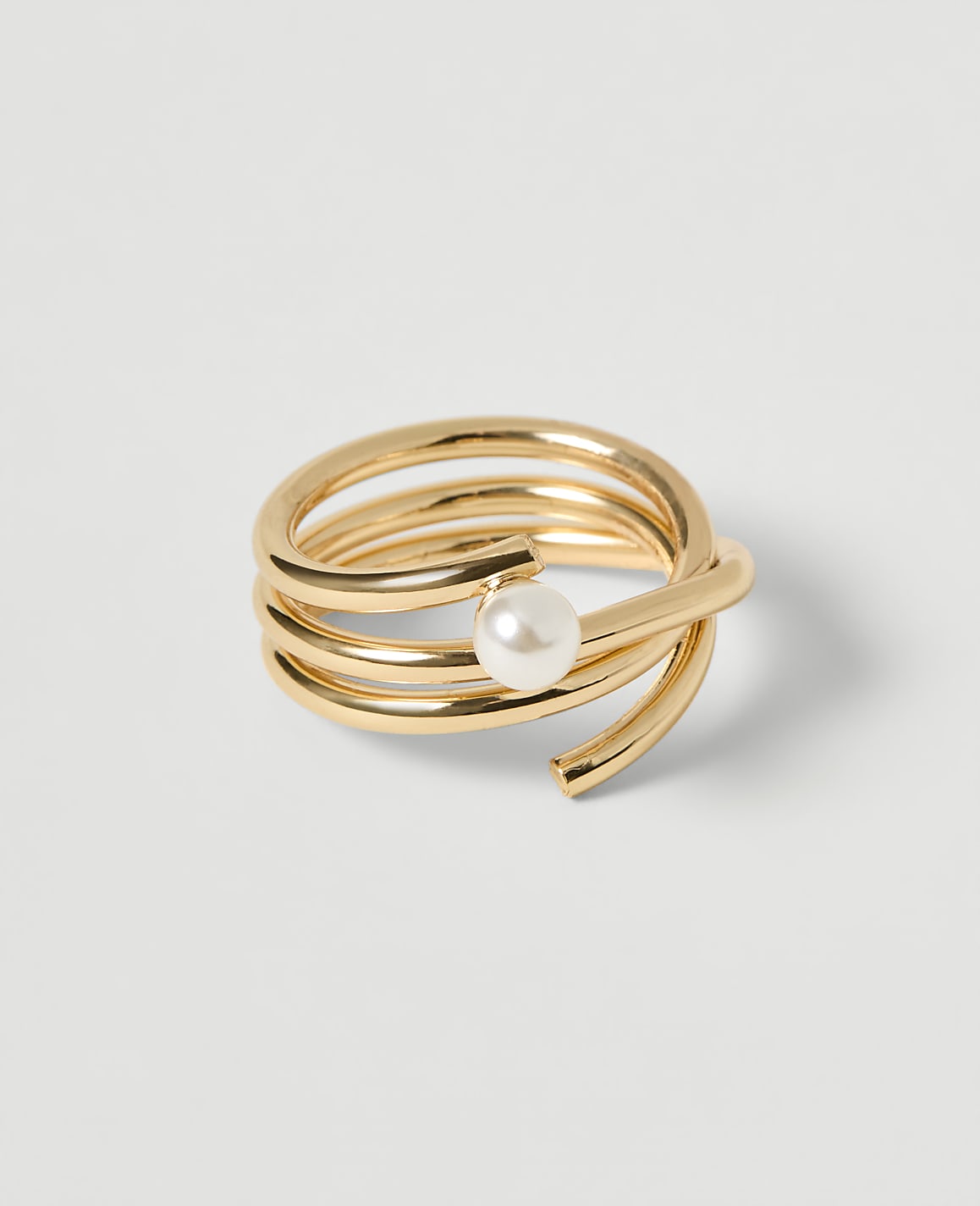 A coiled gold ring with a pearl accent rests on a plain white background.