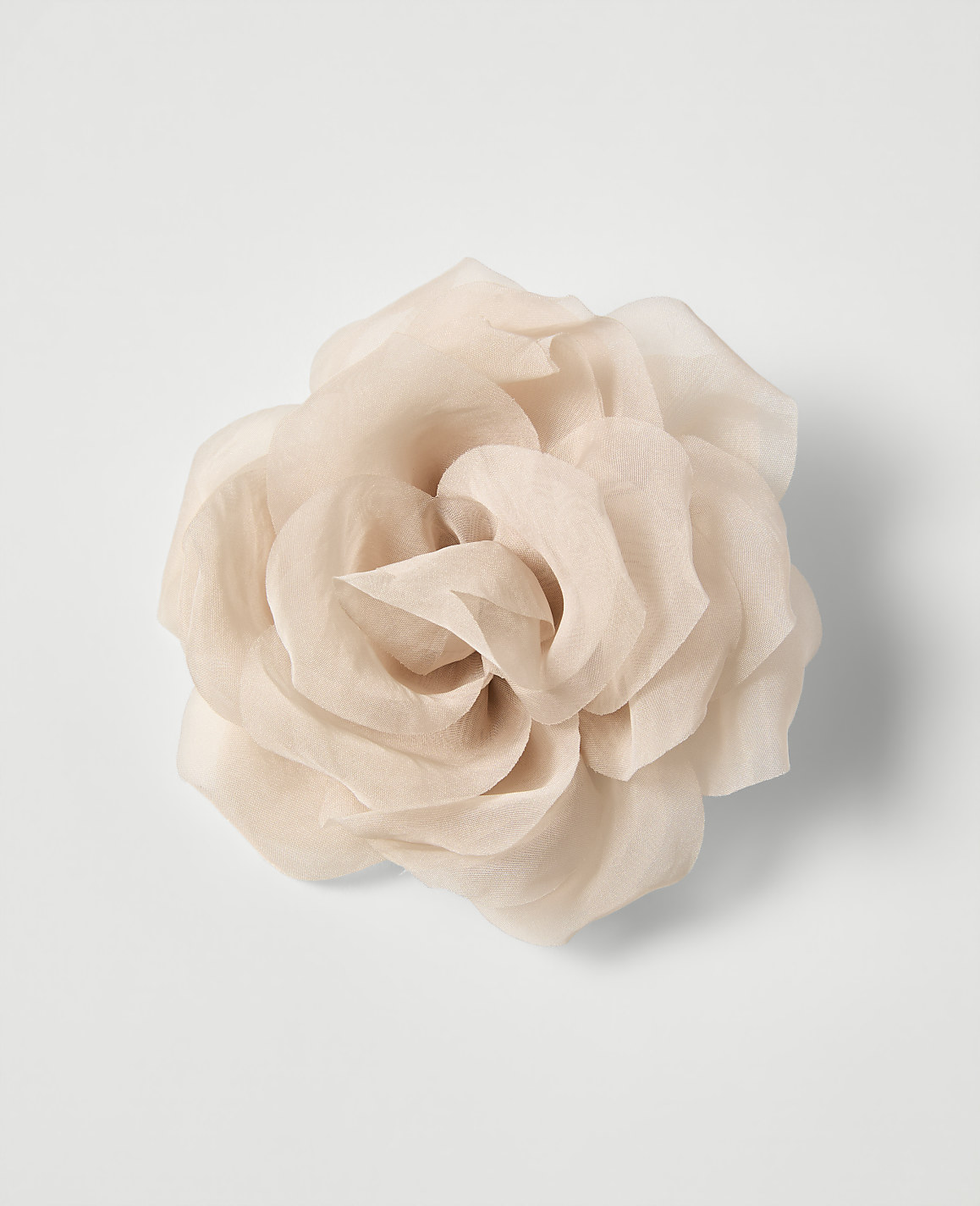 A delicate, pale pink fabric rose with layered petals is centered against a plain white background.