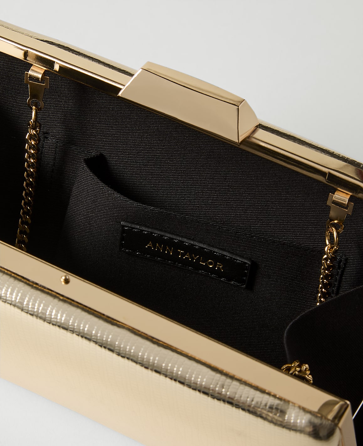 A gold clutch with a textured exterior and a black interior featuring an Ann Taylor label is presented against a plain white background.
