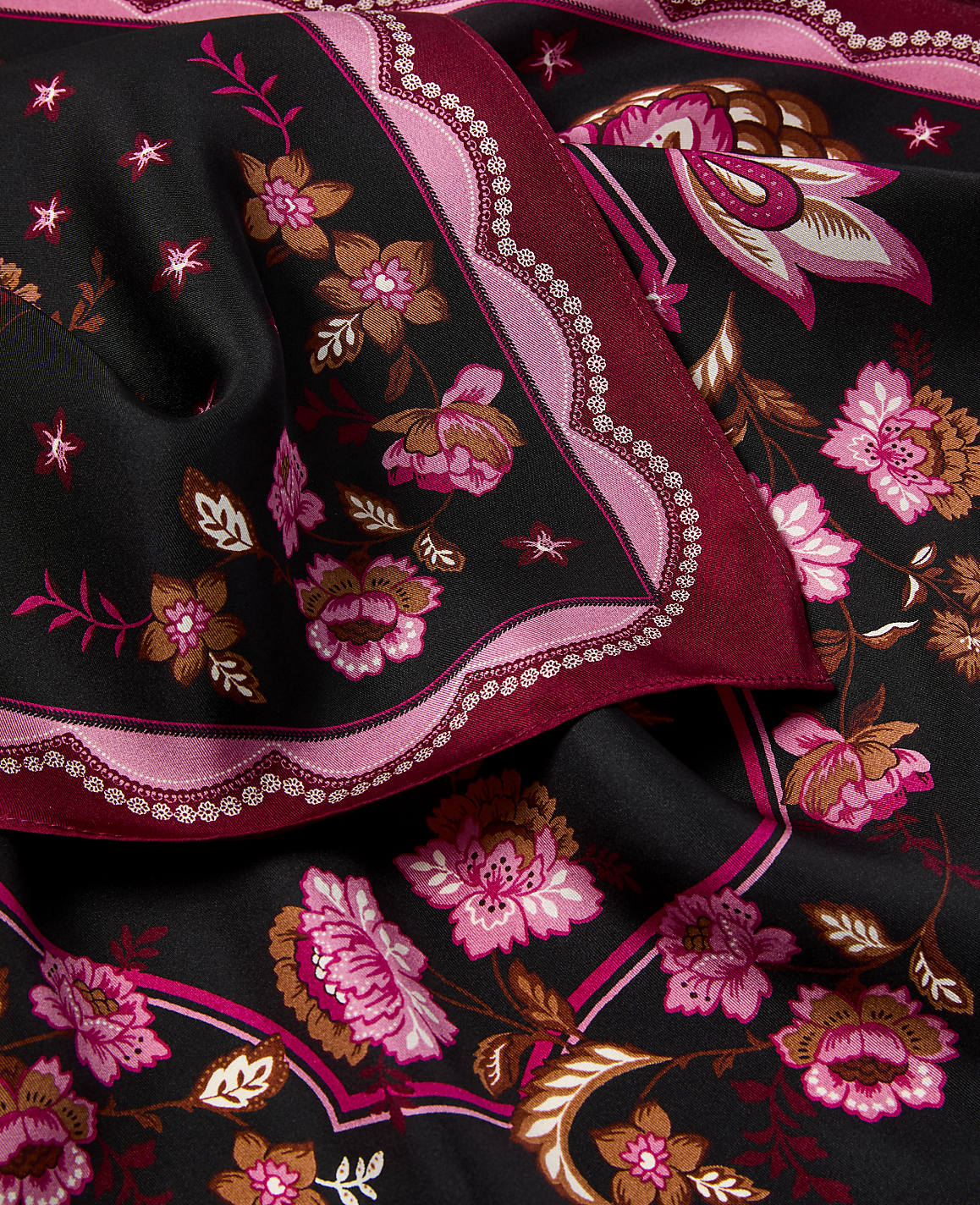 A close-up view of a black fabric with a vibrant floral pattern in shades of pink and brown, featuring a scalloped border.