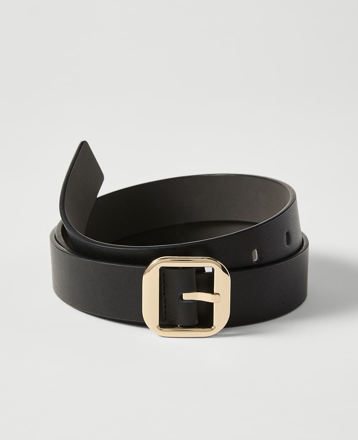A black leather belt with a gold buckle is coiled on a plain white background.