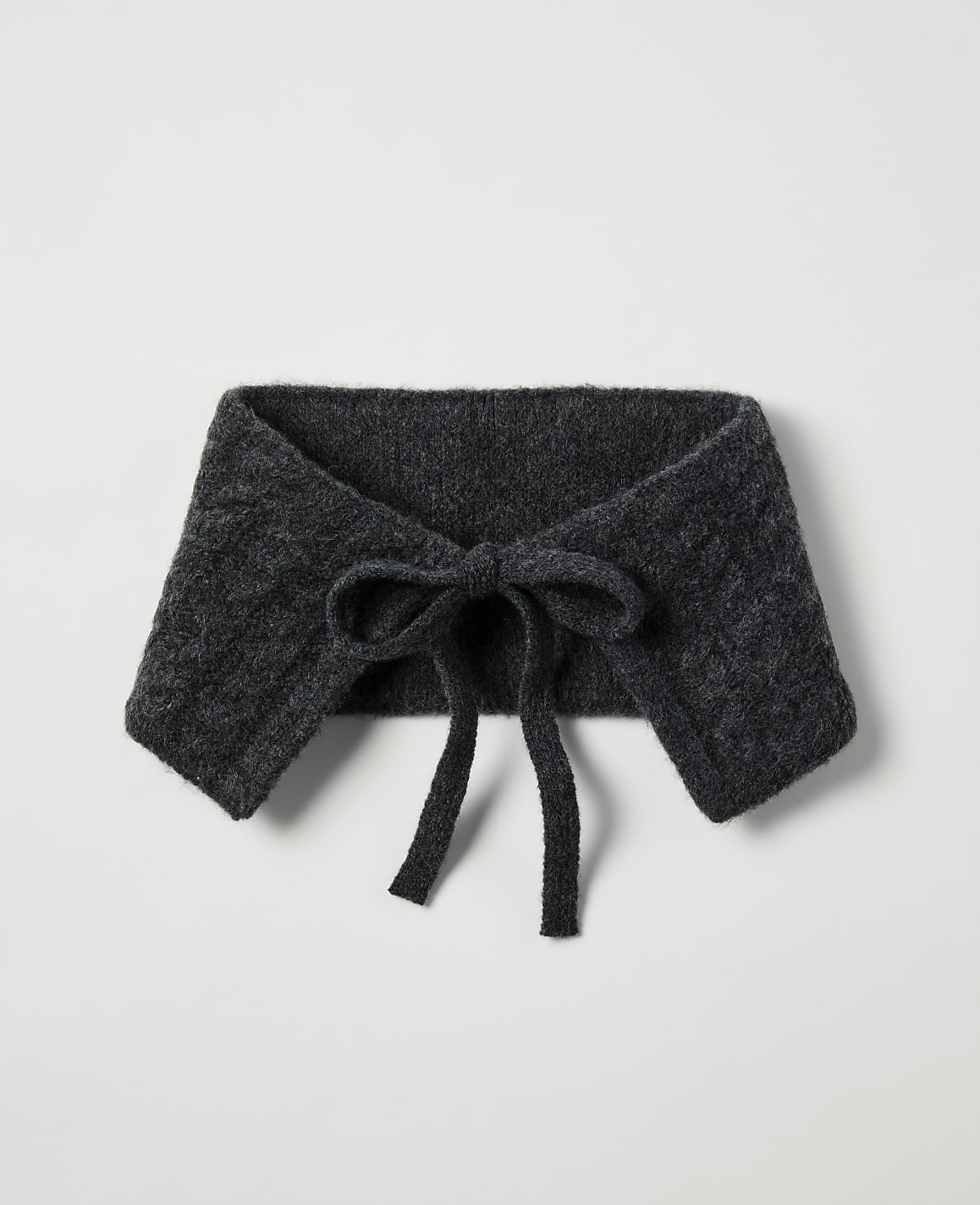A dark gray knitted collar with a bow in the foreground rests on a plain, light gray background.