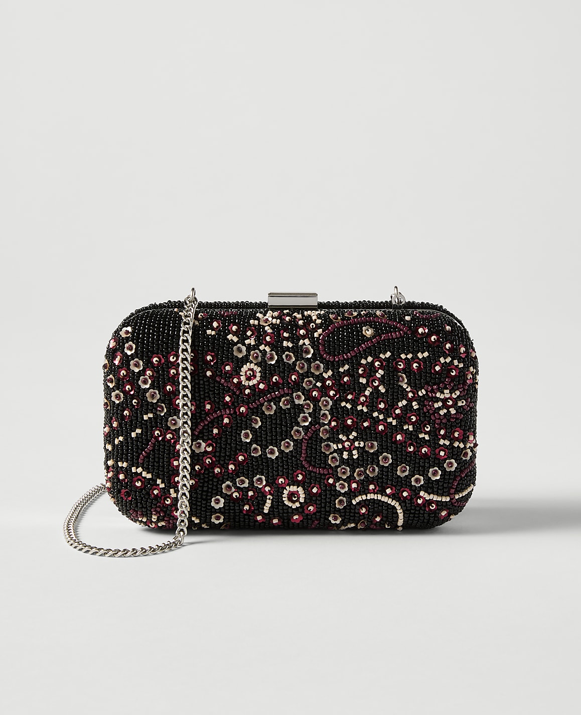 A black beaded clutch with a floral pattern and a silver chain rests against a plain white background.