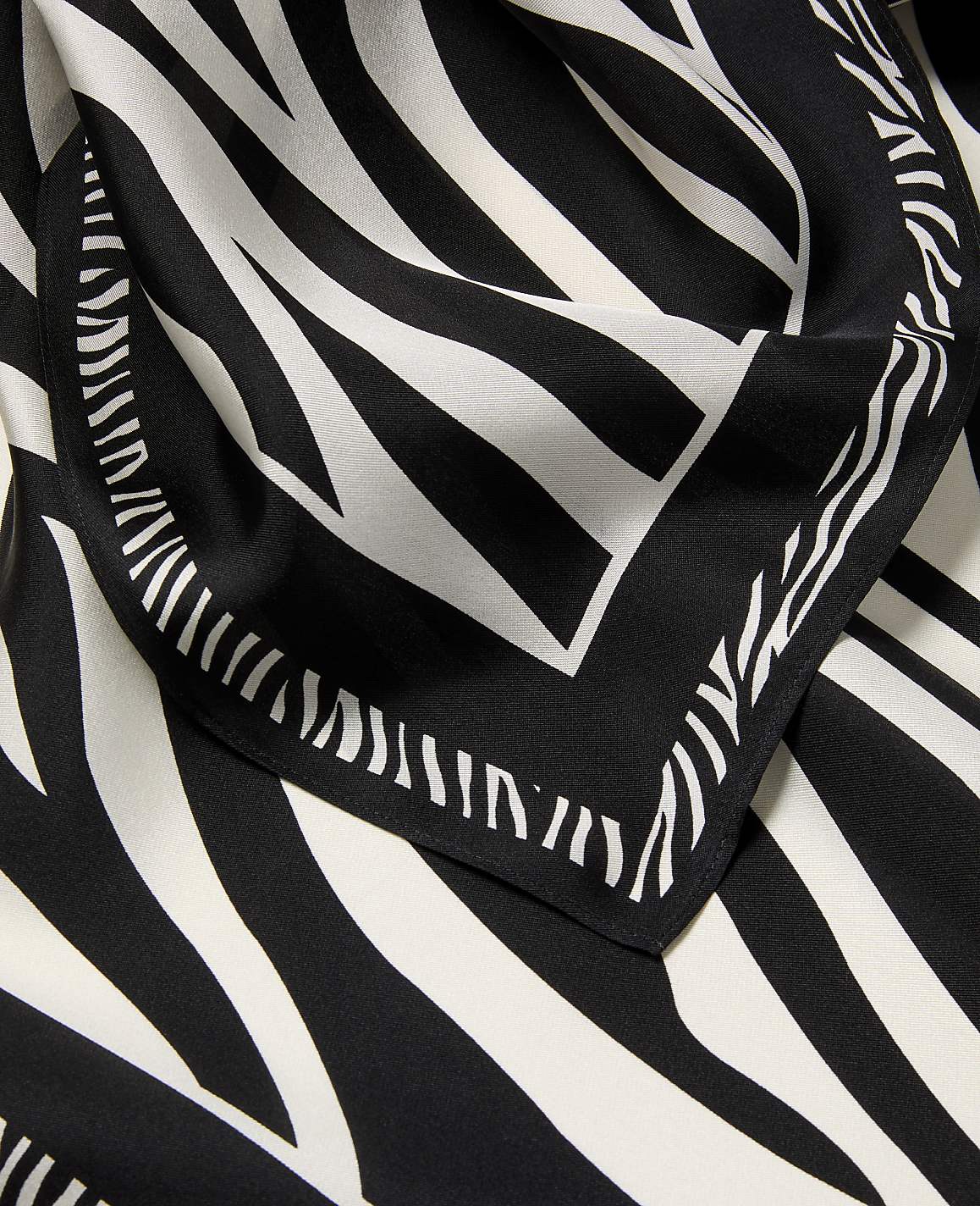 A black and white zebra-print scarf with a decorative border is laid out against a matching patterned background.