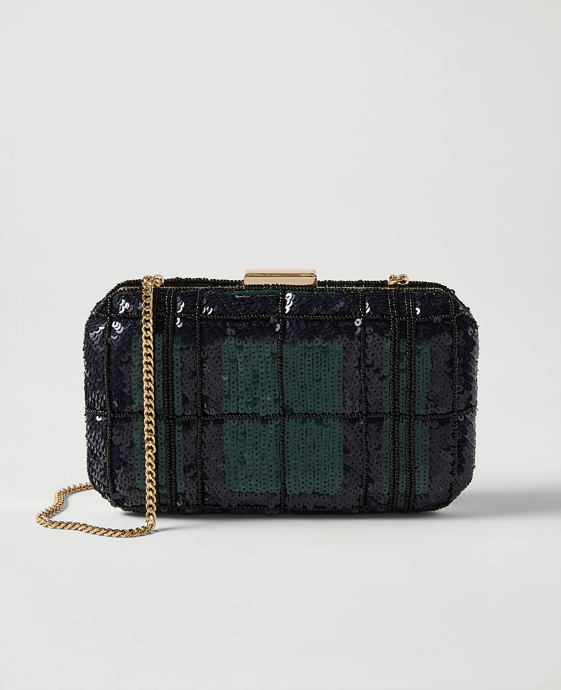 A rectangular clutch purse with a plaid pattern of navy blue and green sequins rests on a white surface, with a gold chain strap draped to the left.