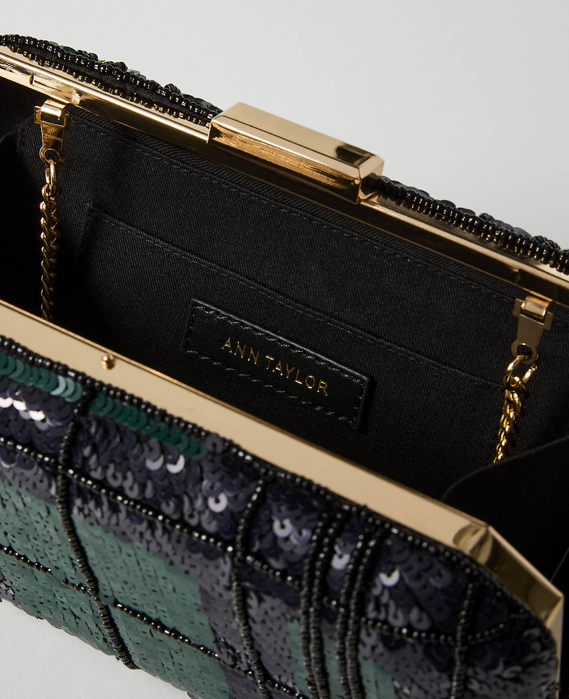 A close-up of an open, sequined clutch purse with a gold clasp and chain, set against a plain white background.