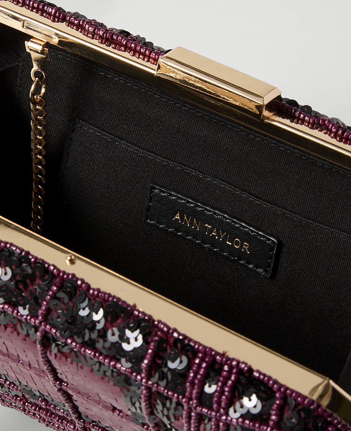 A close-up of an open, sequined clutch with a gold clasp and chain, revealing the Ann Taylor brand tag inside against a dark fabric lining.