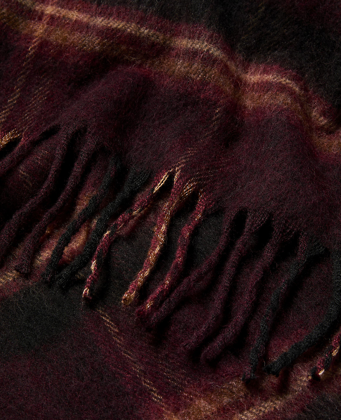A close-up of a burgundy and gold plaid scarf with fringed edges fills the frame.