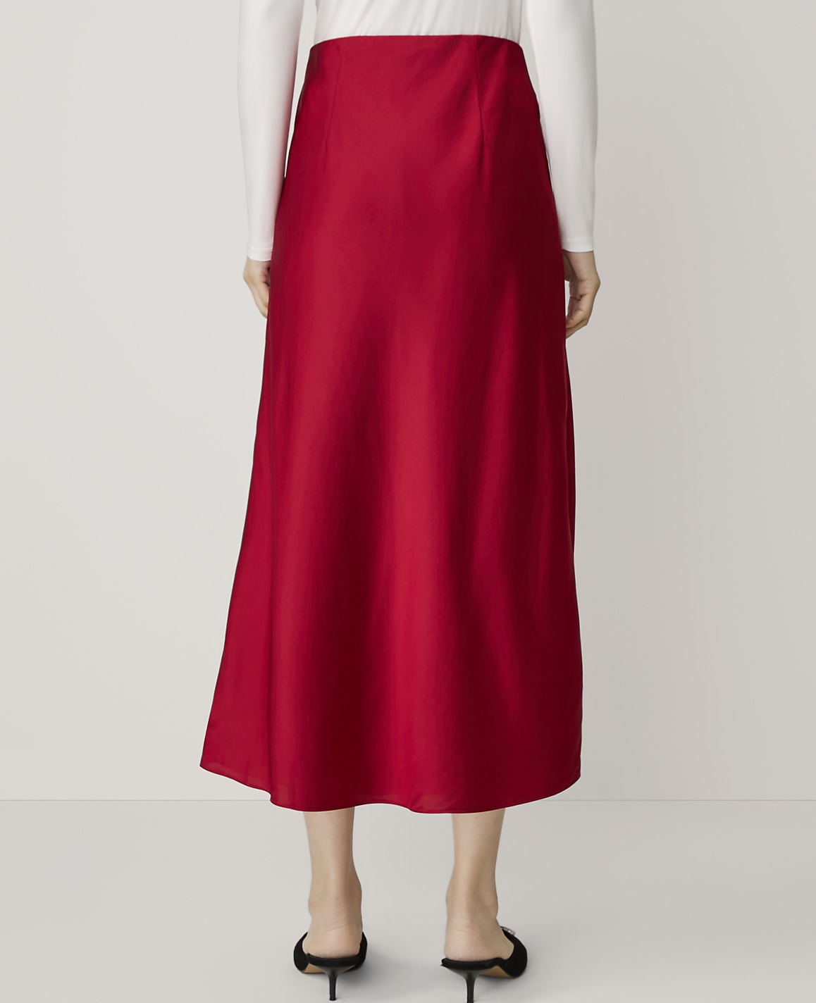 A person wearing a red satin midi skirt and a white long-sleeved top stands against a plain white background.