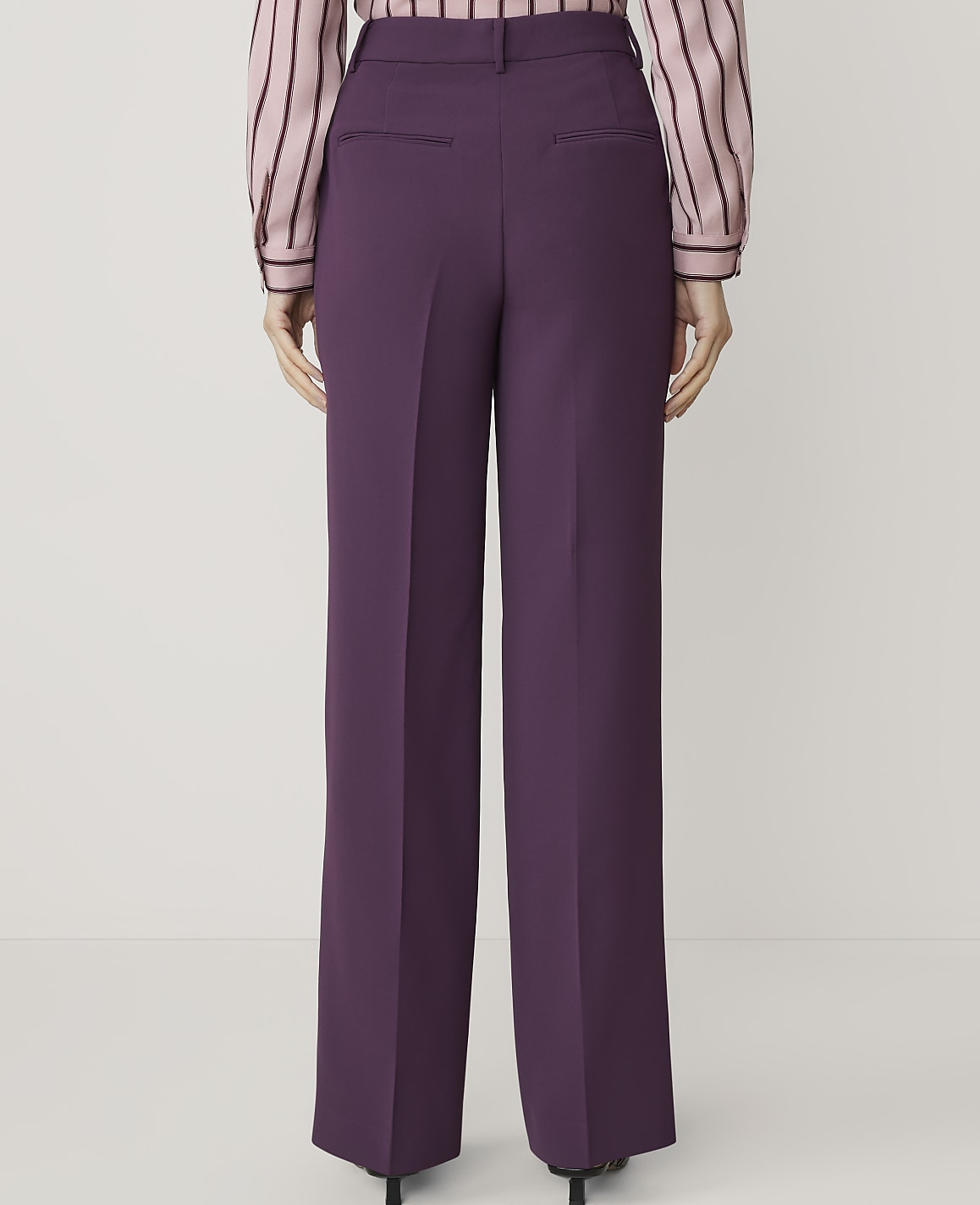 A person wearing purple wide-leg trousers and a striped blouse stands against a plain white background.