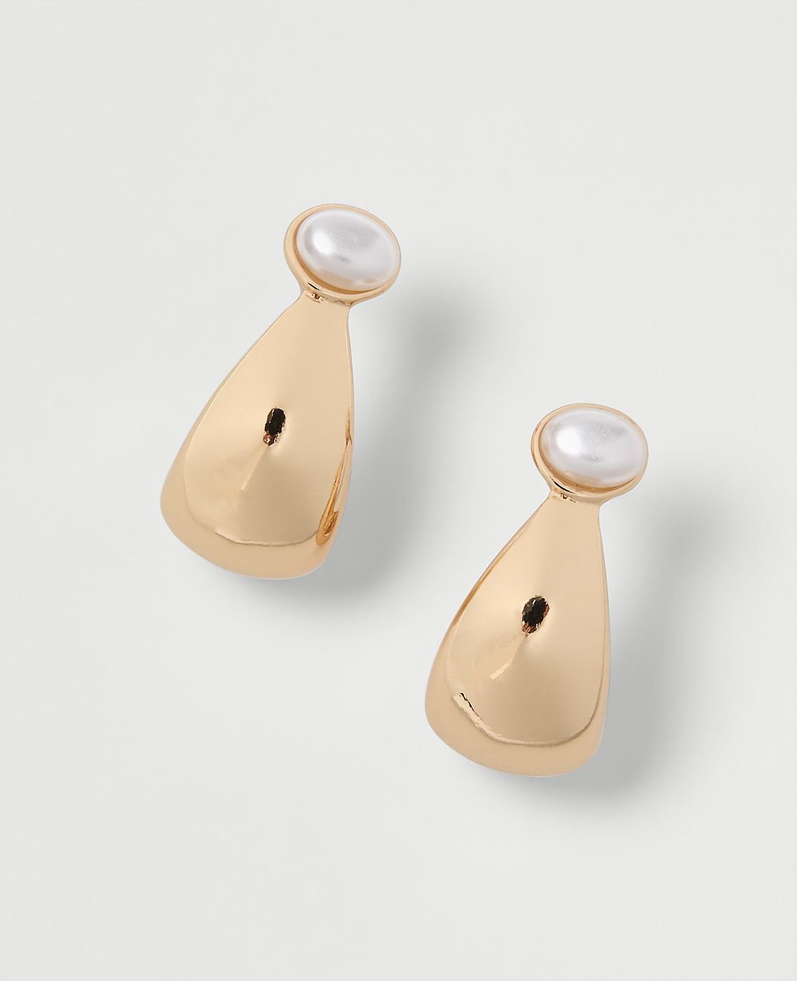 A pair of gold teardrop earrings with pearl accents rests on a plain white background.
