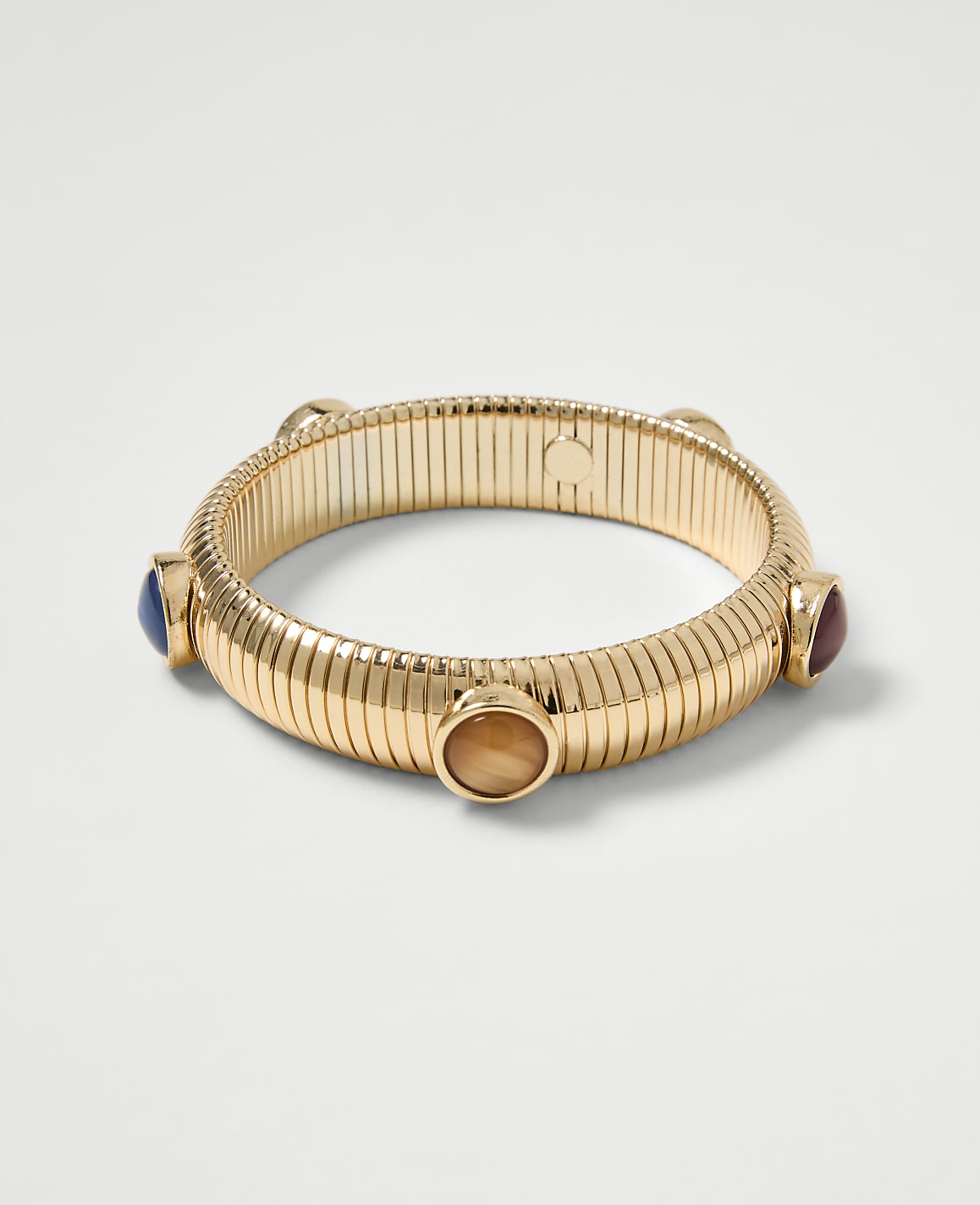 A gold ribbed bangle with four colorful cabochon stones is displayed against a plain white background.
