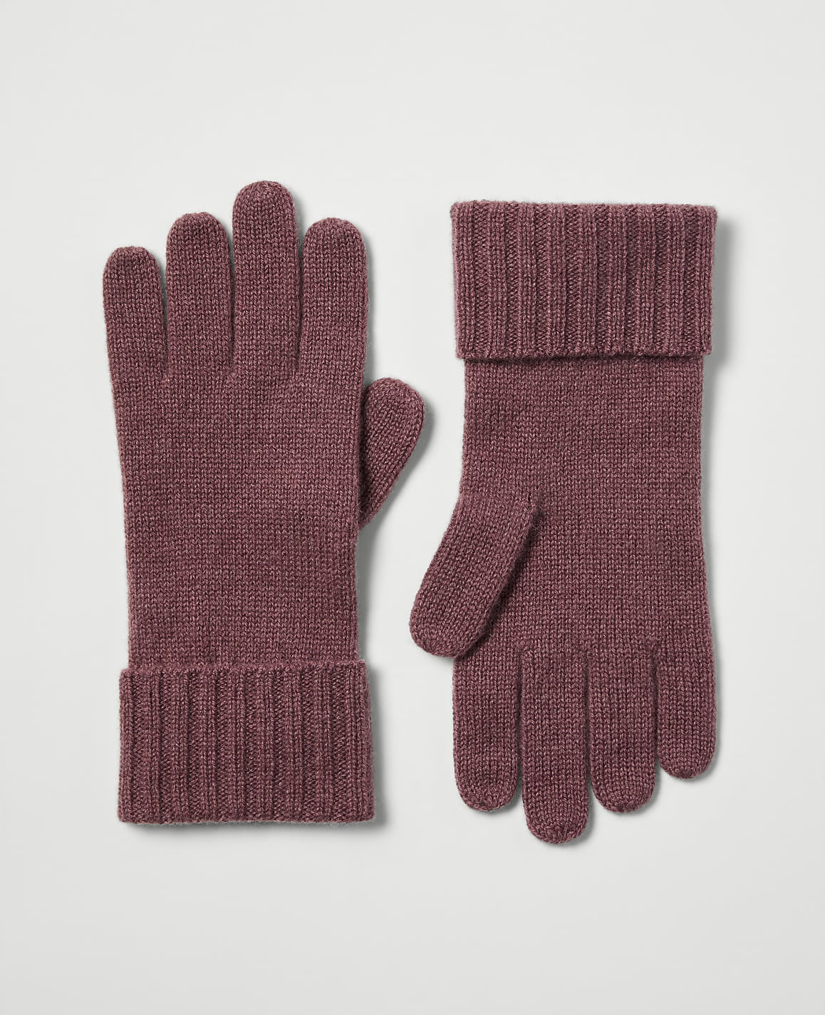 A pair of rose-colored knit gloves with ribbed cuffs rests on a plain, light gray background.