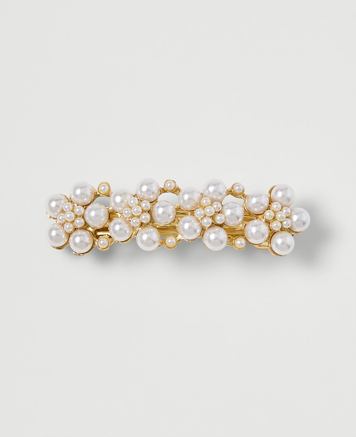A gold barrette adorned with clusters of pearls sits on a plain, light-colored background.