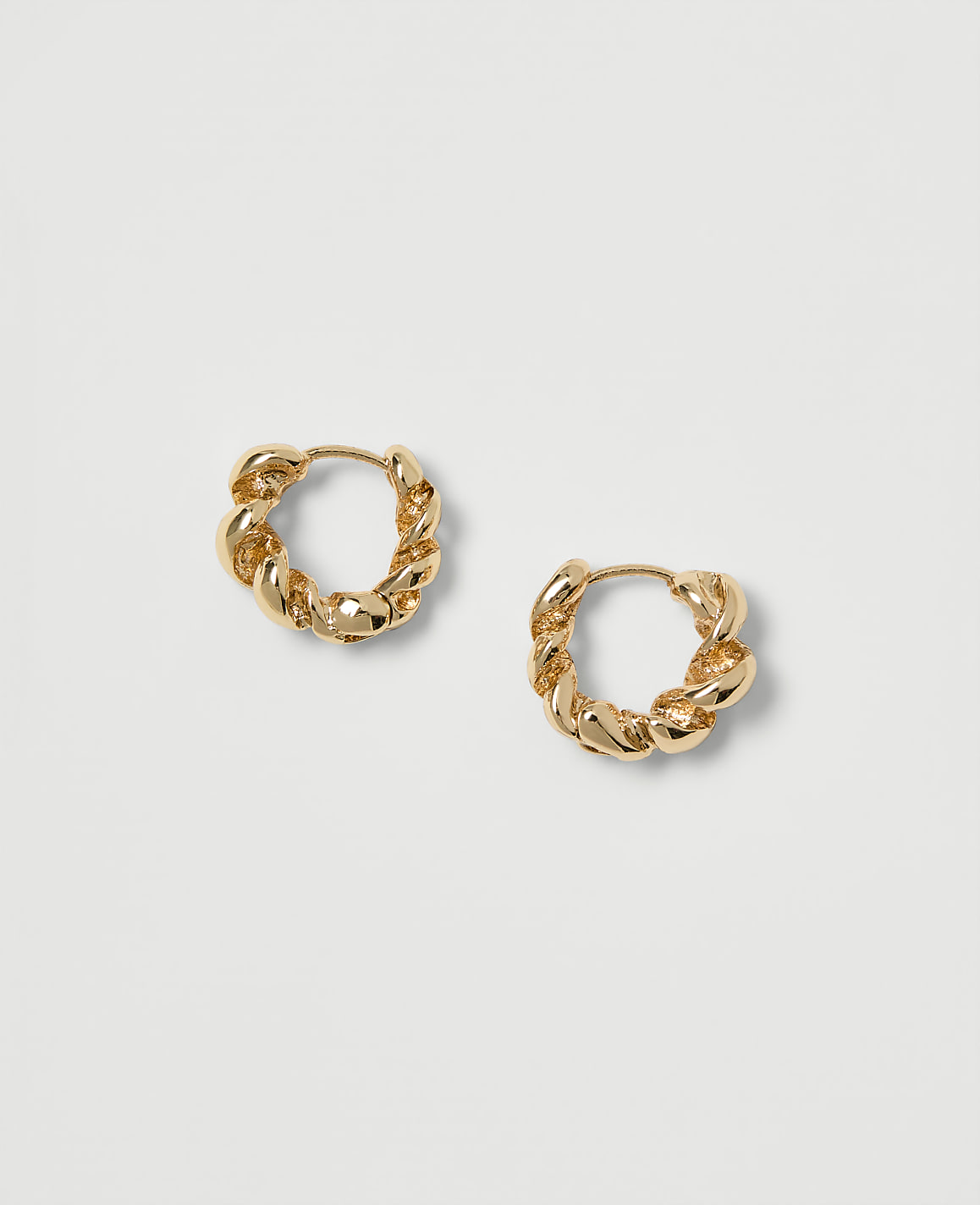 Two gold twisted hoop earrings rest on a plain, light gray background.