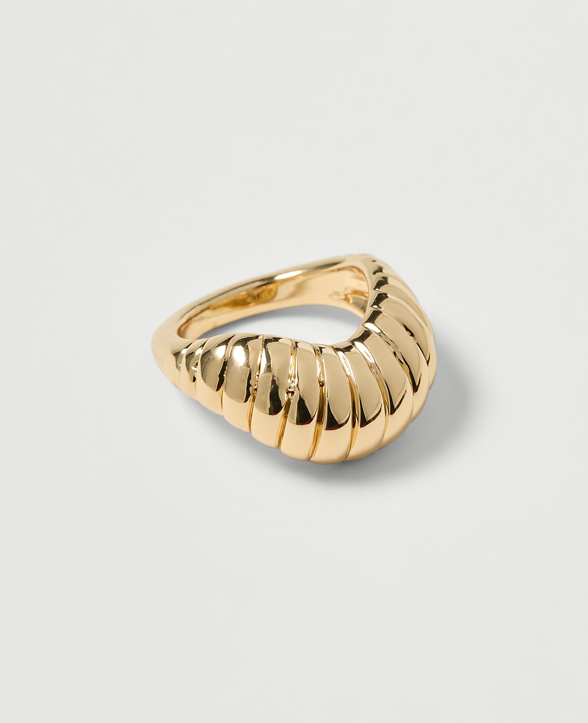A gold ring with a ribbed, curved design rests on a plain, light gray background.