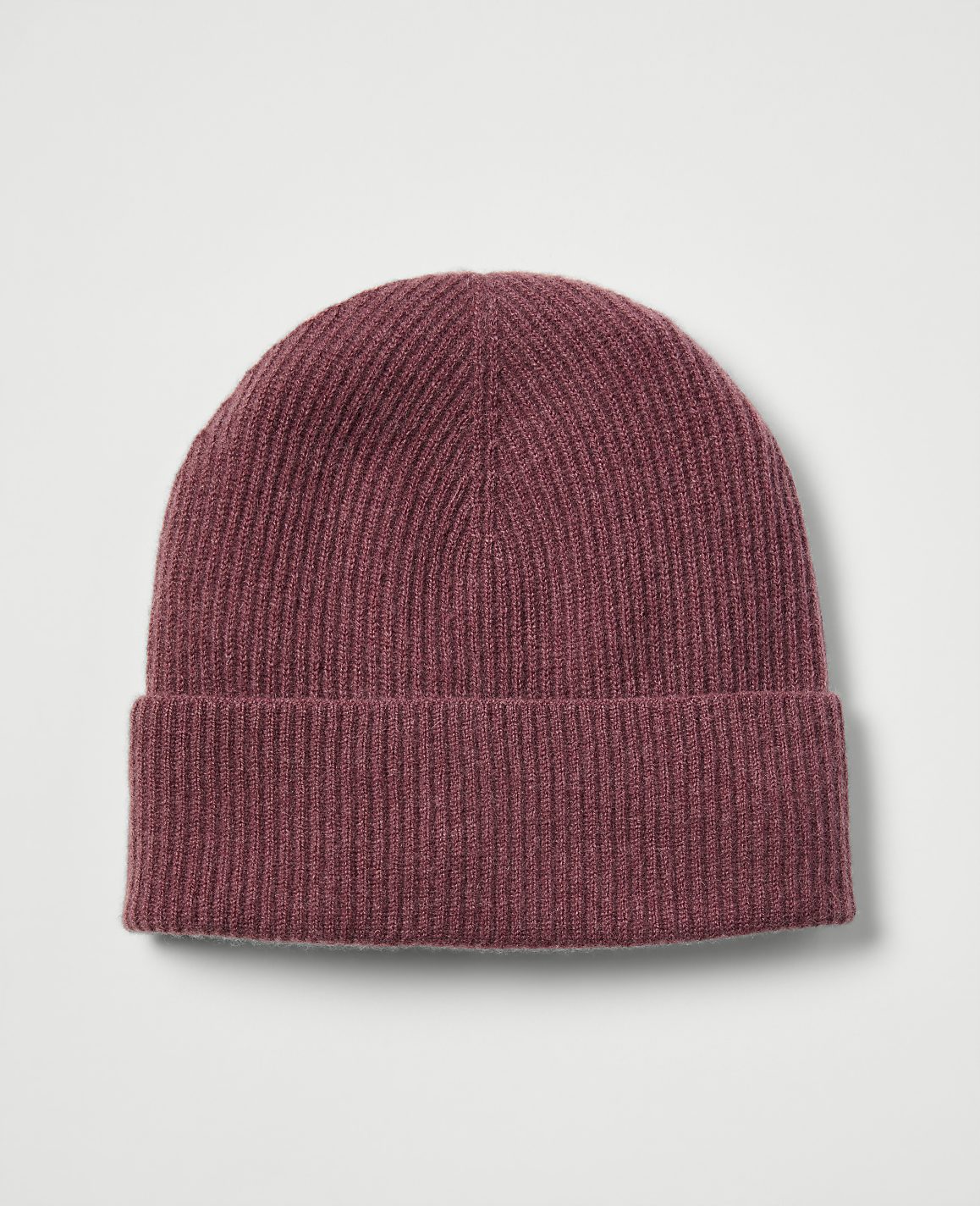A maroon ribbed beanie with a folded brim rests against a plain, light gray background.