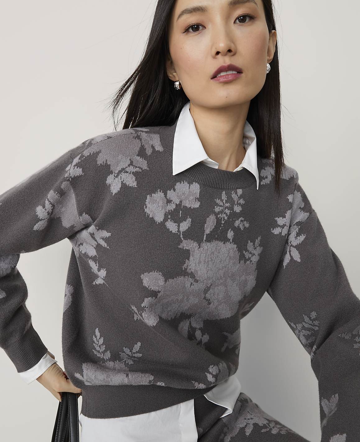 A woman in a floral sweater and white shirt is shown against a plain background.