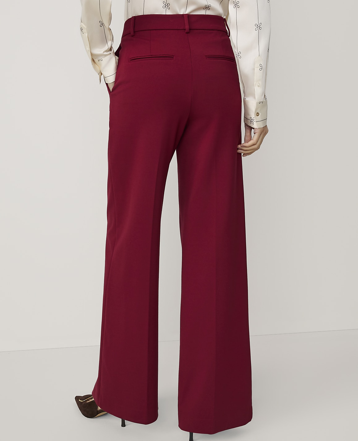 A person wearing wide-leg burgundy pants and a patterned blouse stands against a plain white background.