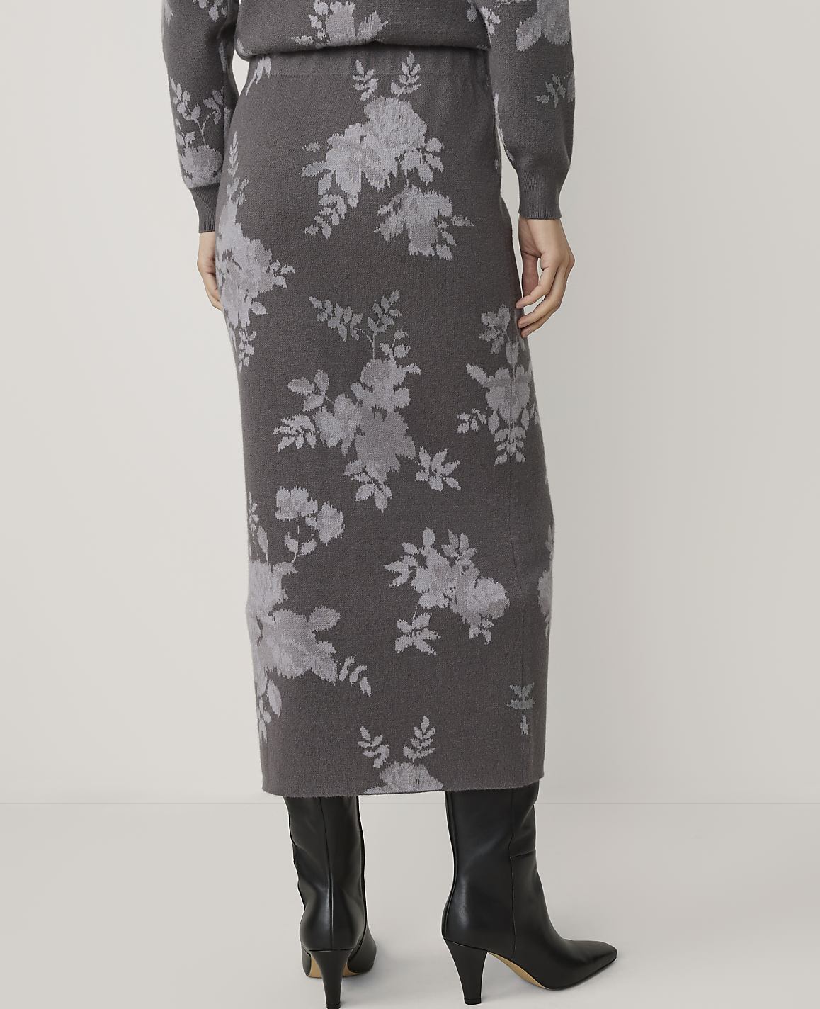 A person wearing a floral print skirt and black boots stands against a plain background.