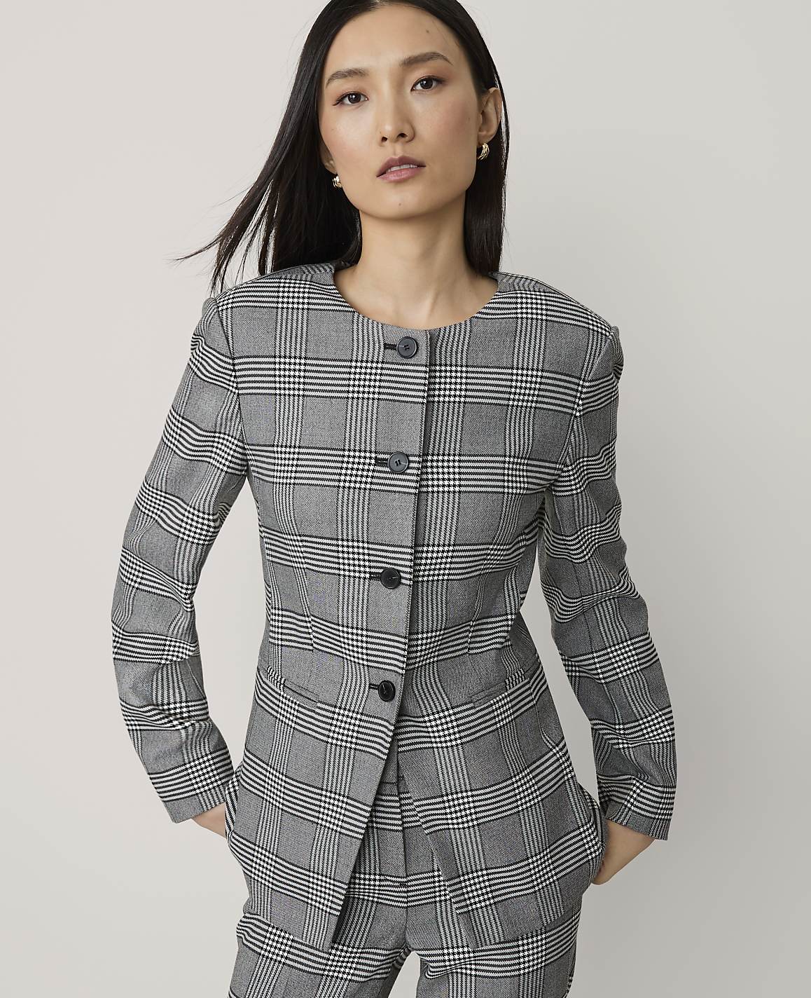 A woman in a plaid suit stands against a plain white background.