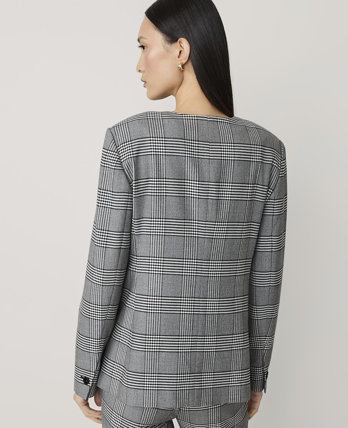 A woman in a plaid blazer and pants stands against a plain, light gray background.