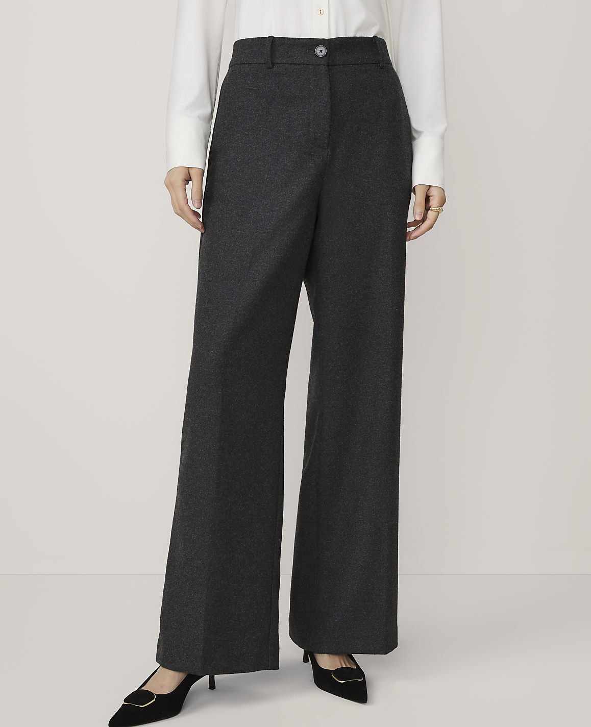 A person in a white shirt and dark grey wide-leg trousers stands against a plain white background.
