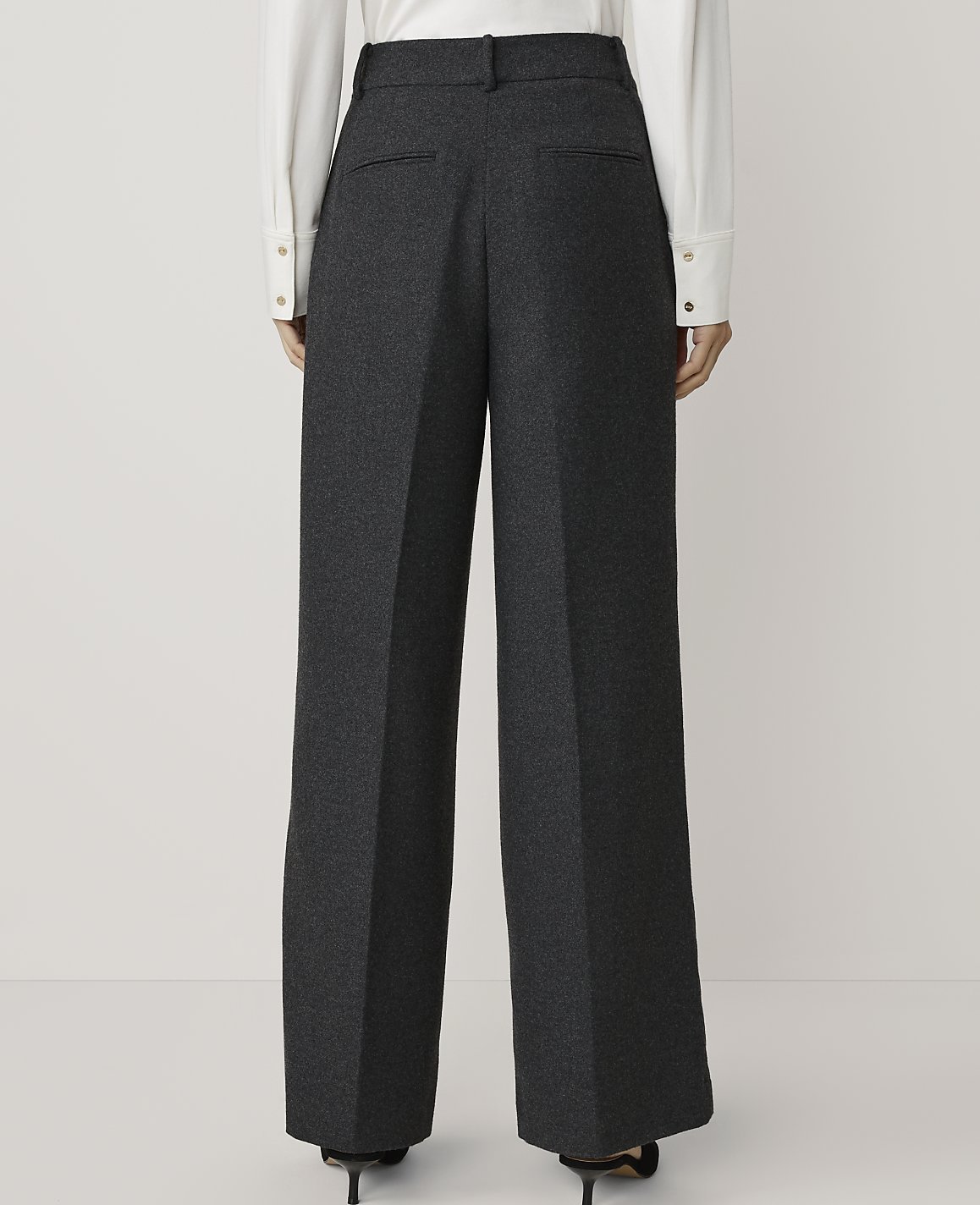 A person stands in dark grey wide-leg trousers and a white shirt against a plain white background.