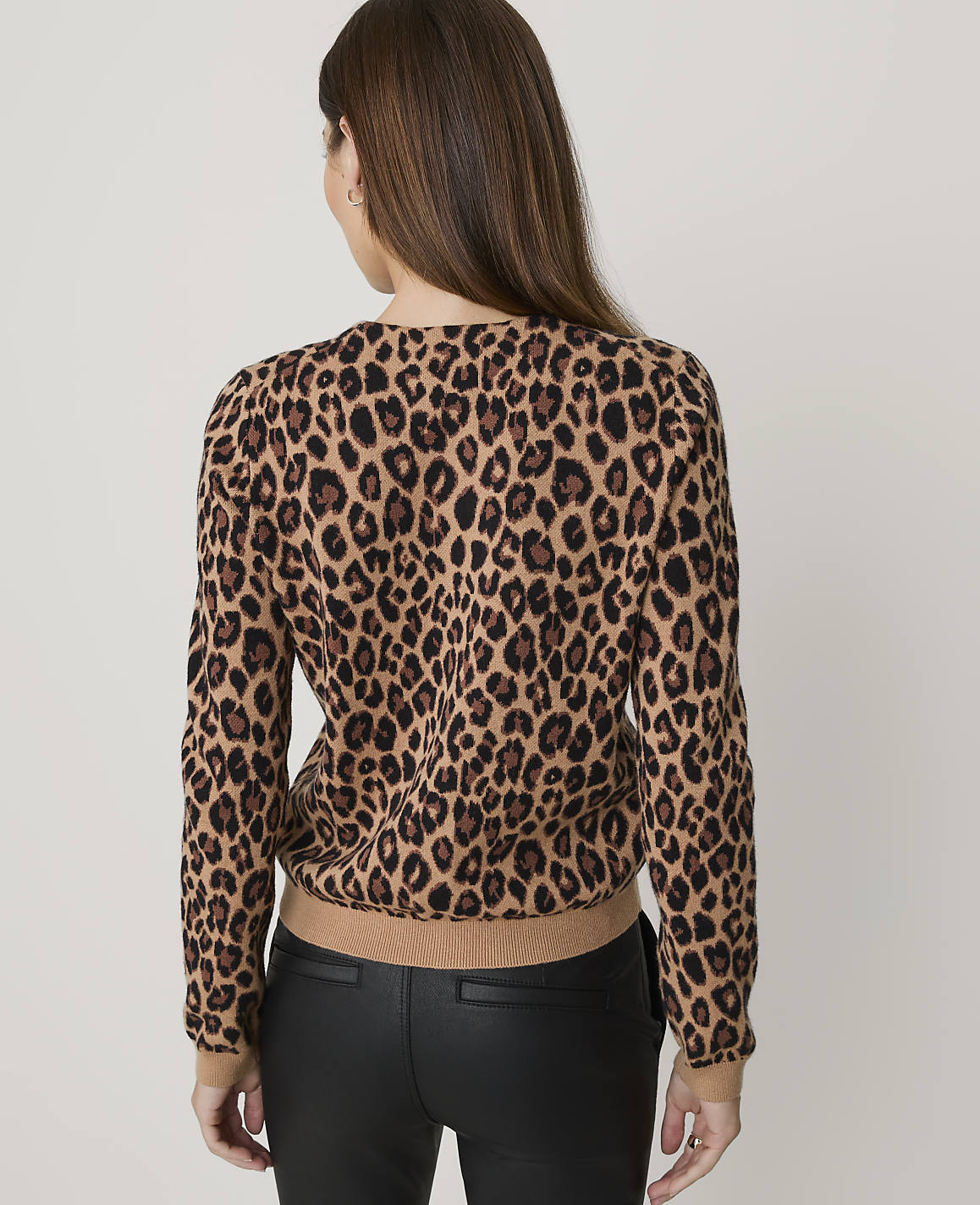 A woman in a leopard print sweater and black pants stands against a plain white background.