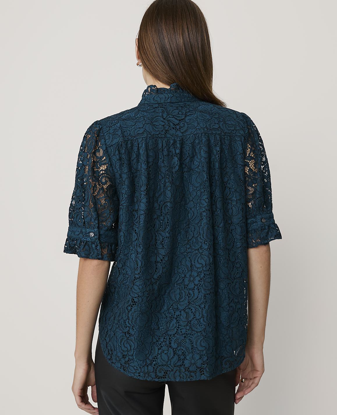 A woman in a teal lace blouse stands against a plain white background.