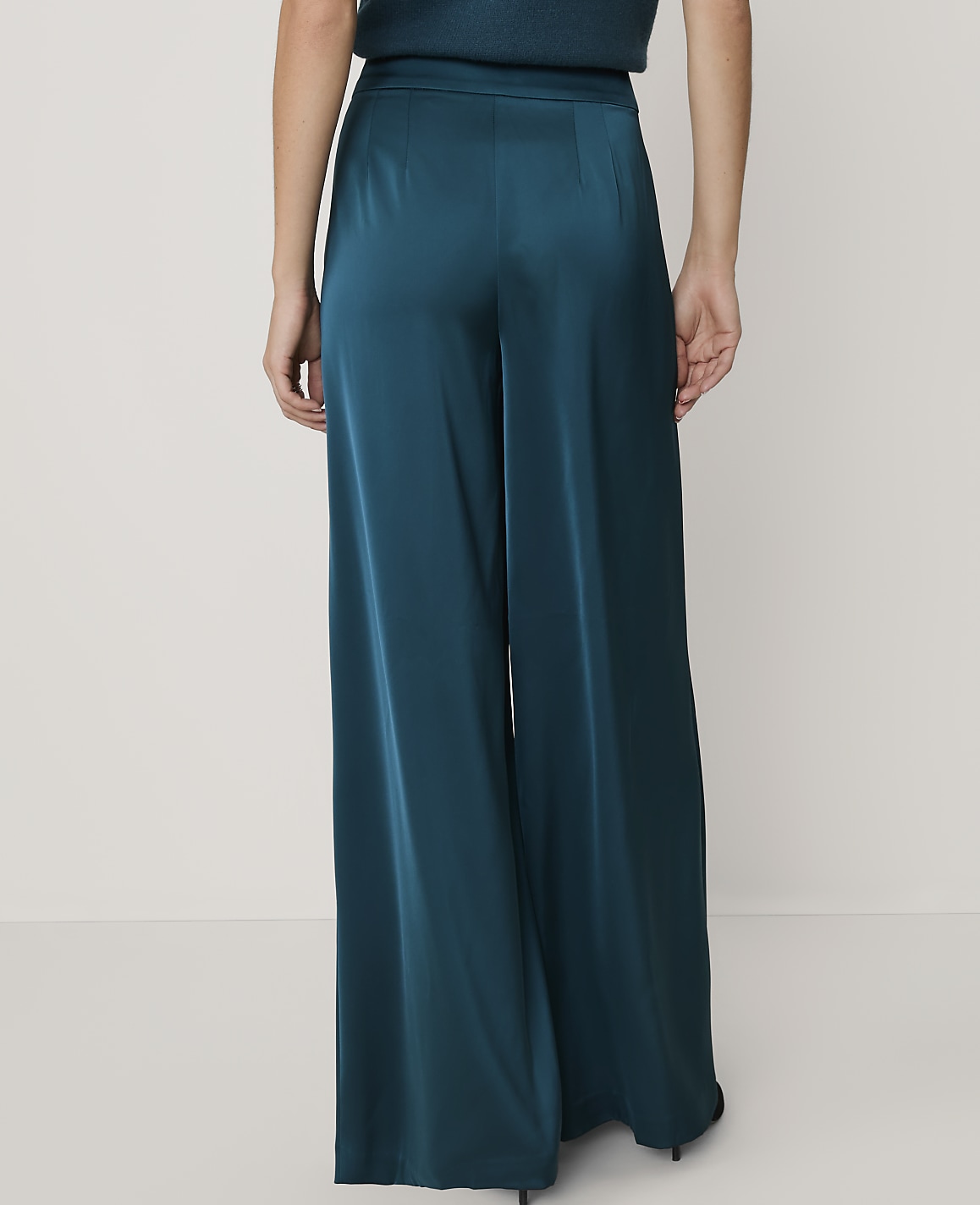 A person stands in teal satin wide-leg pants against a plain white background.