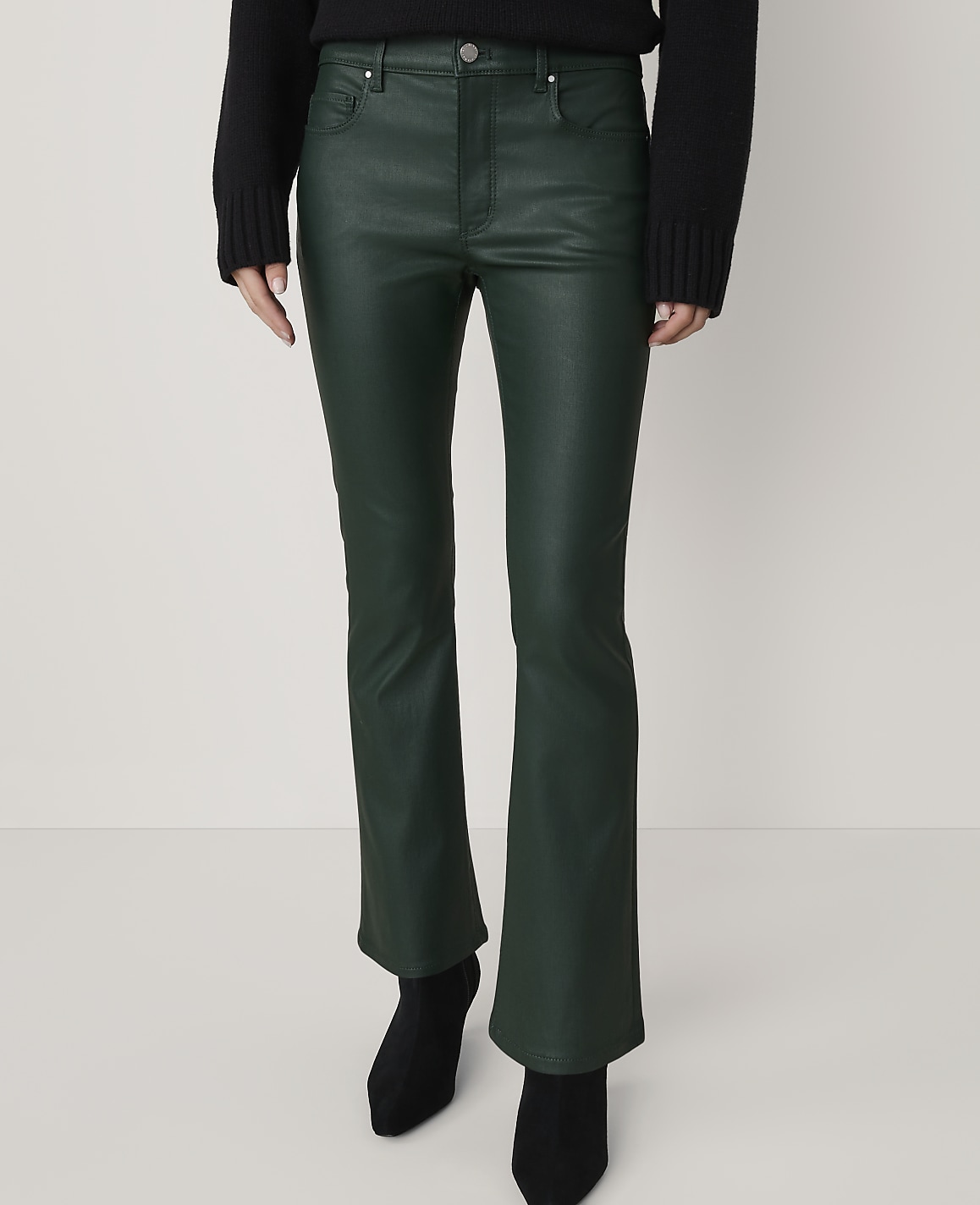 A person stands in dark green flared pants and black boots against a plain, light-colored background.