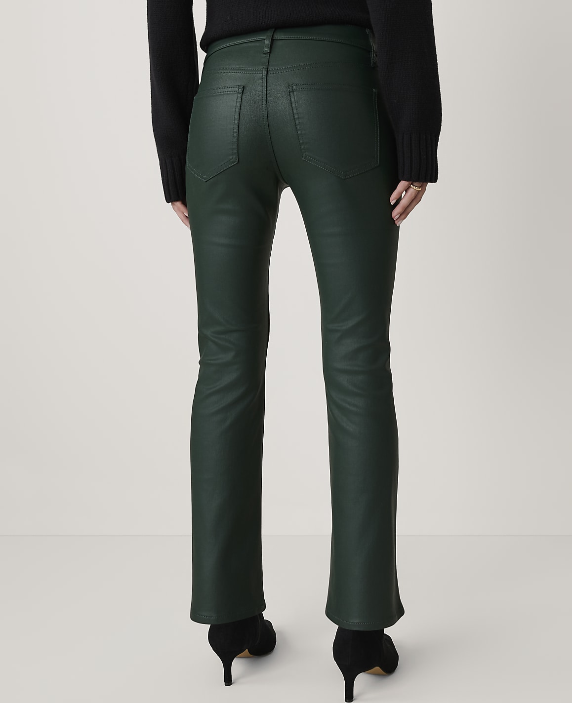 A person wearing dark green, flared pants and black heels stands against a plain white background.