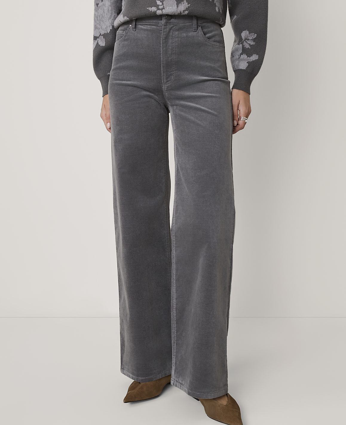 A person stands in gray corduroy wide-leg pants and a floral sweater against a plain gray background.