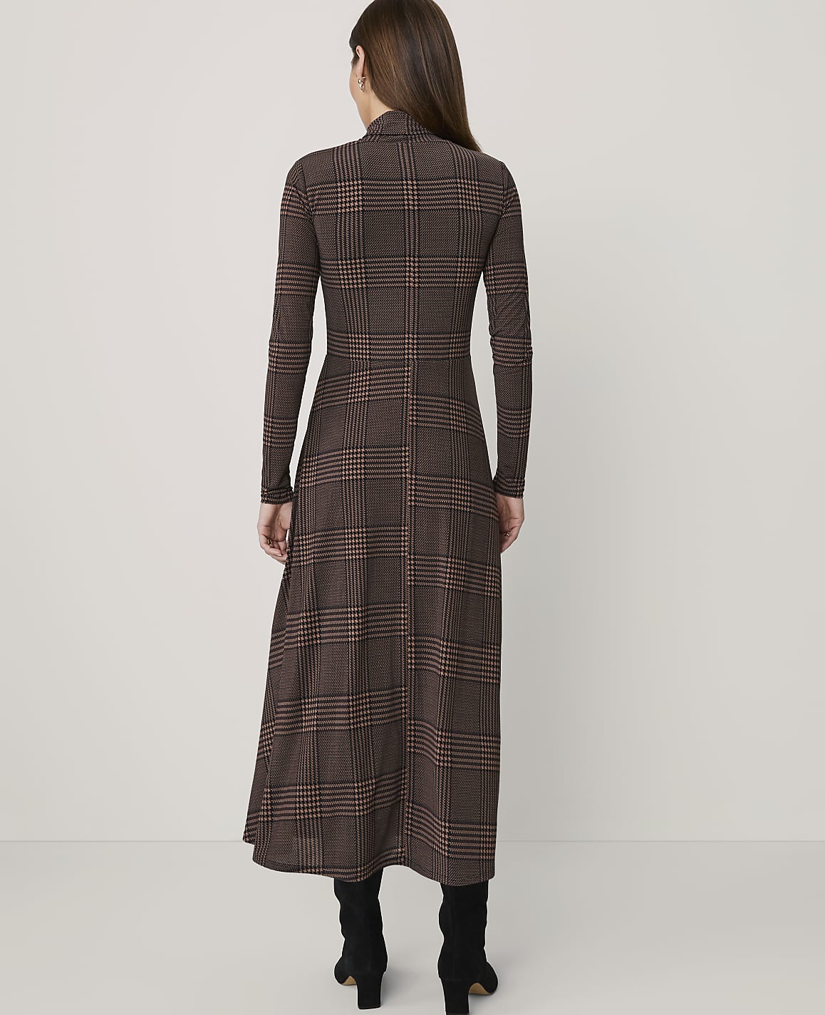 A woman in a brown plaid dress stands against a plain white background.