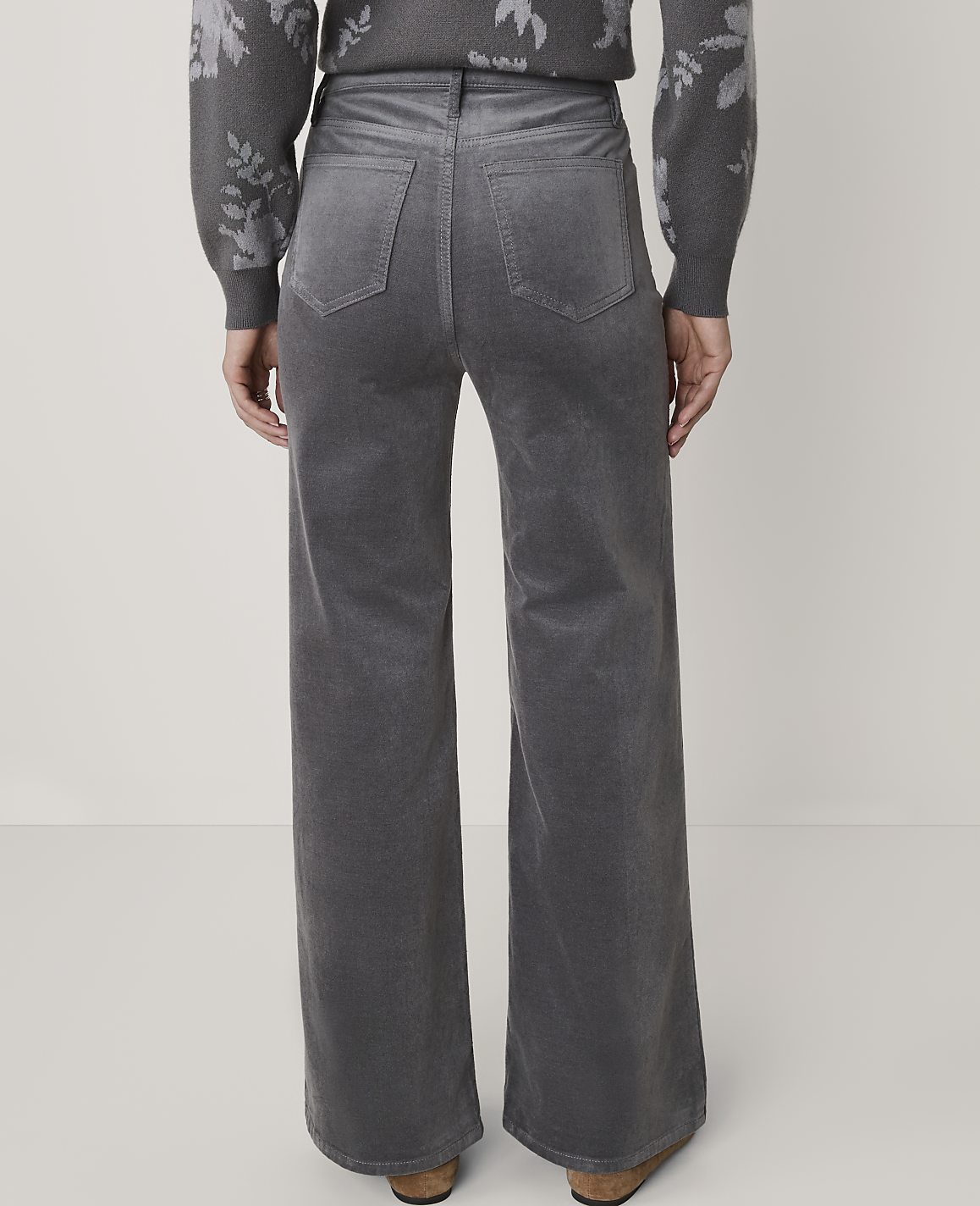 A person wearing gray corduroy wide-leg pants and a patterned sweater stands against a plain white background.