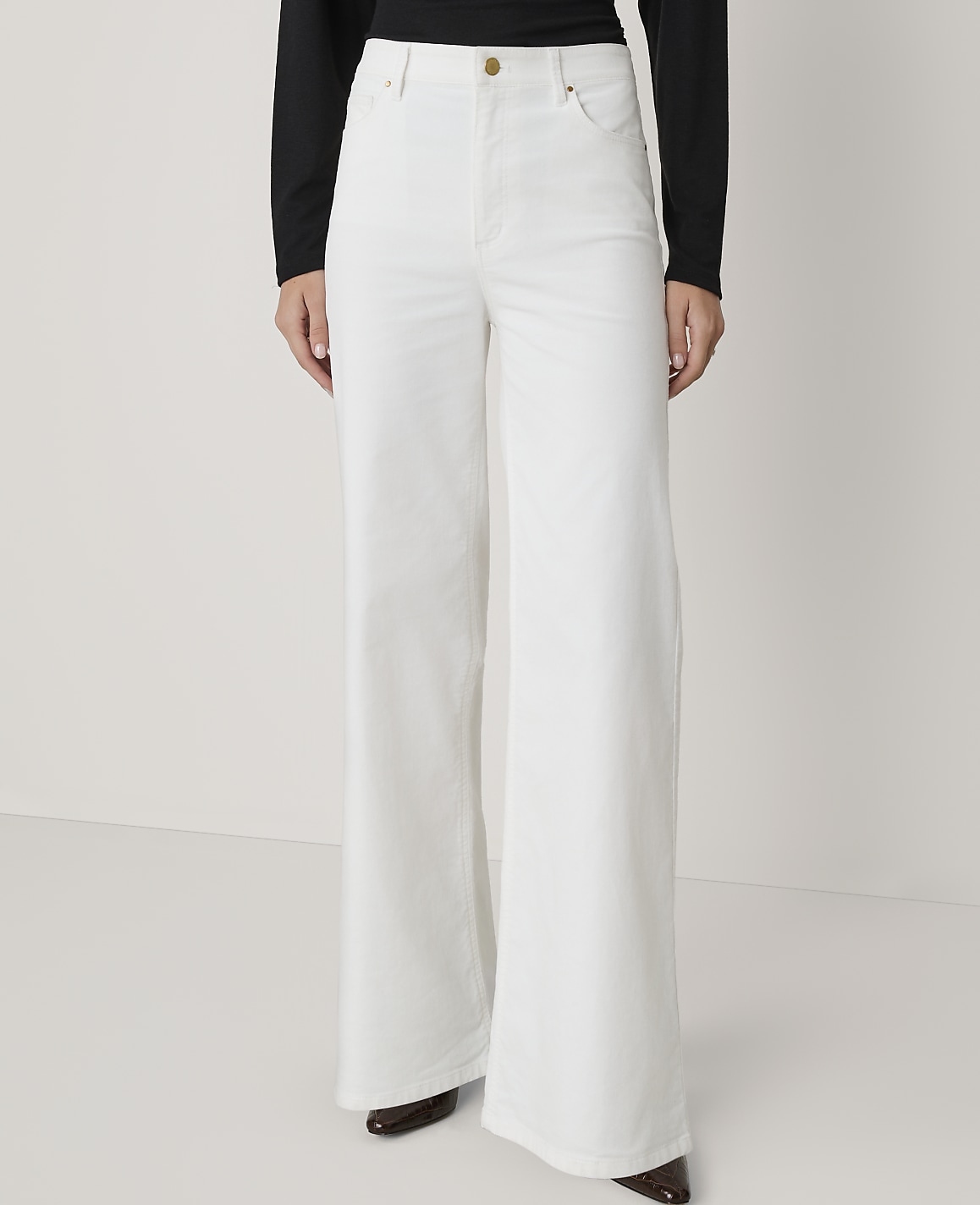 A person stands in white wide-leg jeans and a black top against a plain white background.