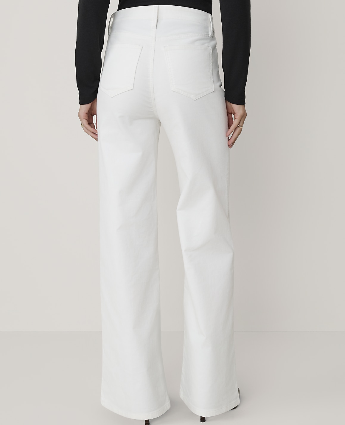 A person wearing white wide-leg jeans stands against a plain white background.