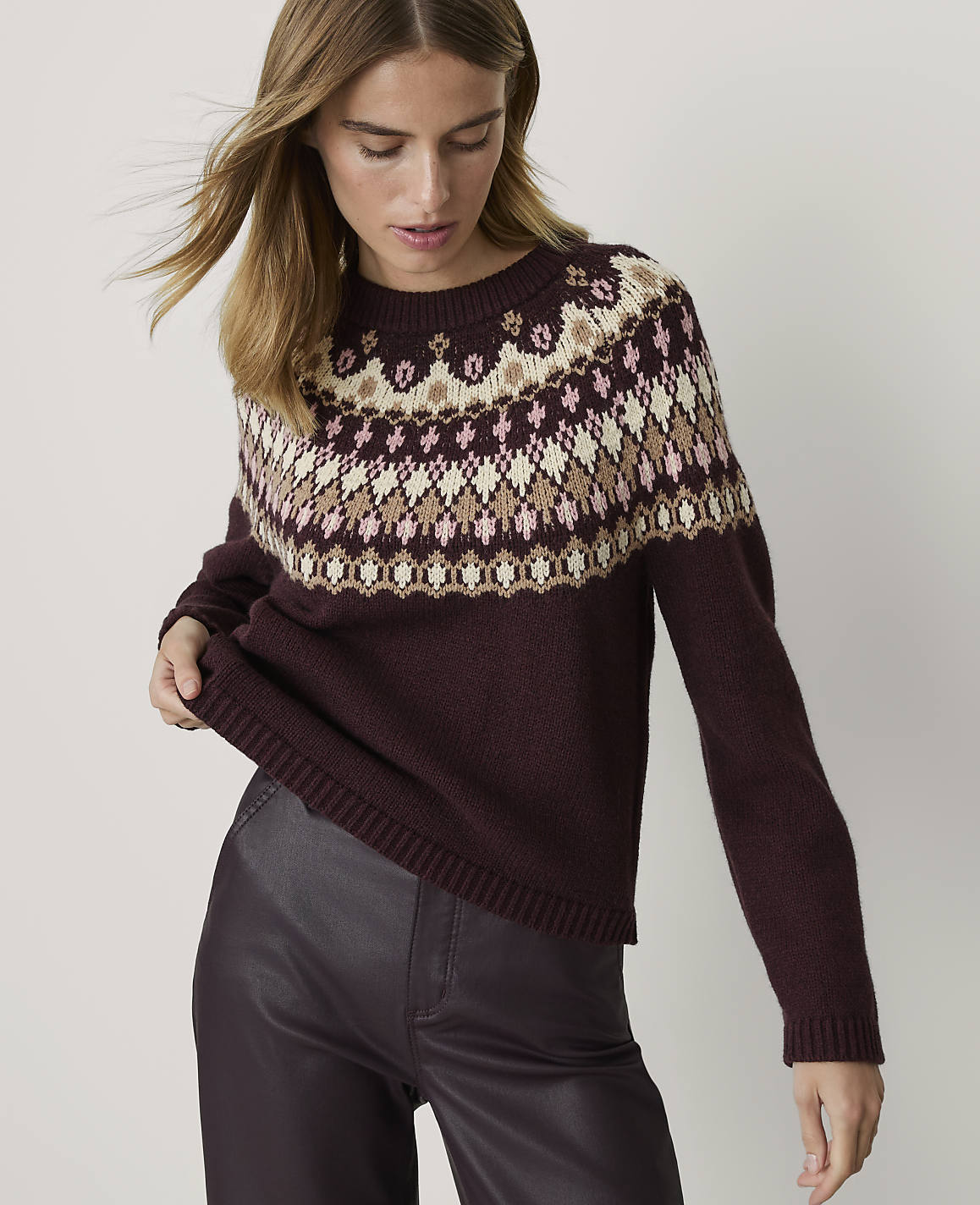 A woman in a burgundy sweater with a fair isle pattern stands against a plain white background.