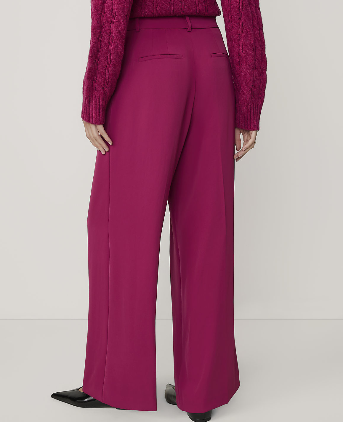 A person wearing a magenta sweater and matching wide-leg pants stands against a plain white background.