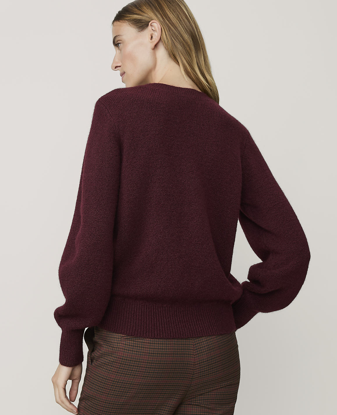 A woman in a maroon sweater and plaid pants stands against a plain white background.