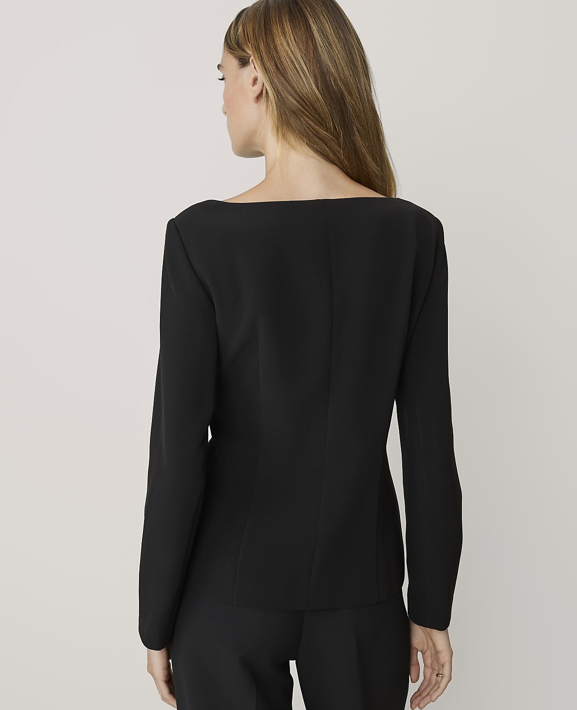 A woman in a black blazer and pants stands against a plain, light gray background.